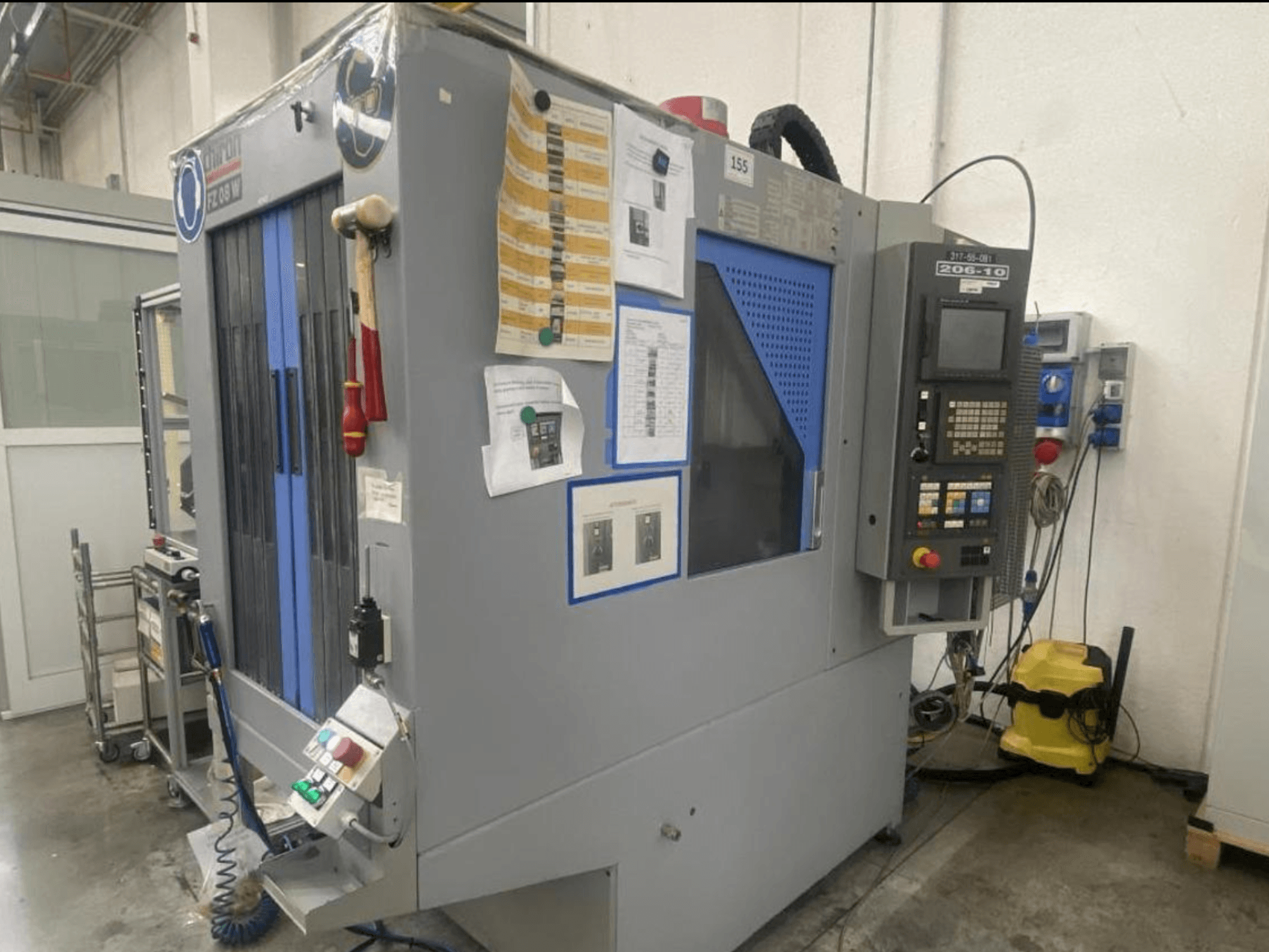 Máquina CNC de Shin Lin, vista frontal, con panel de control, botones de funcionamiento e instrucciones de seguridad adjuntas.