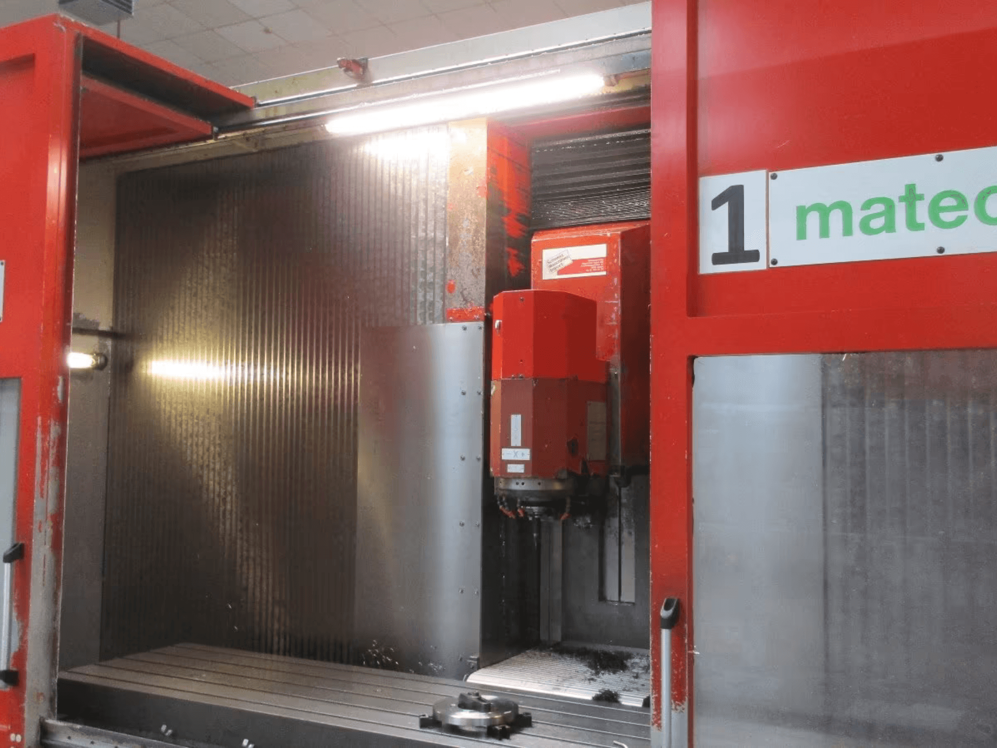 Vista frontal del Centro de Mecanizado Vertical CNC Matec 30 HV con herramienta de corte visible, superficie metálica y detalles del interior de la máquina.