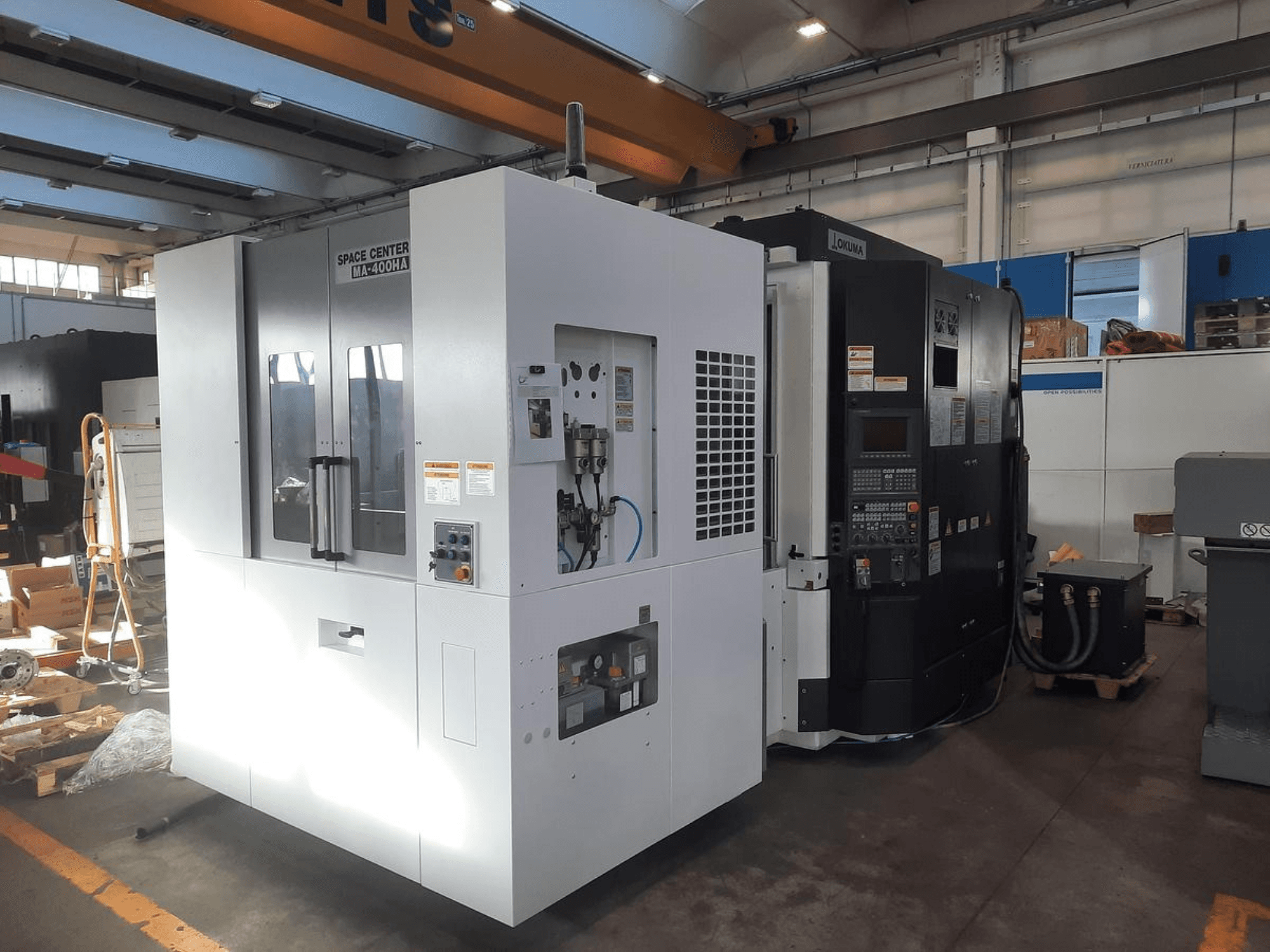Vista frontal de las máquinas CNC SPACE CENTER IM-400HAA y OKUMA, mostrando varios controles y etiquetas del fabricante.