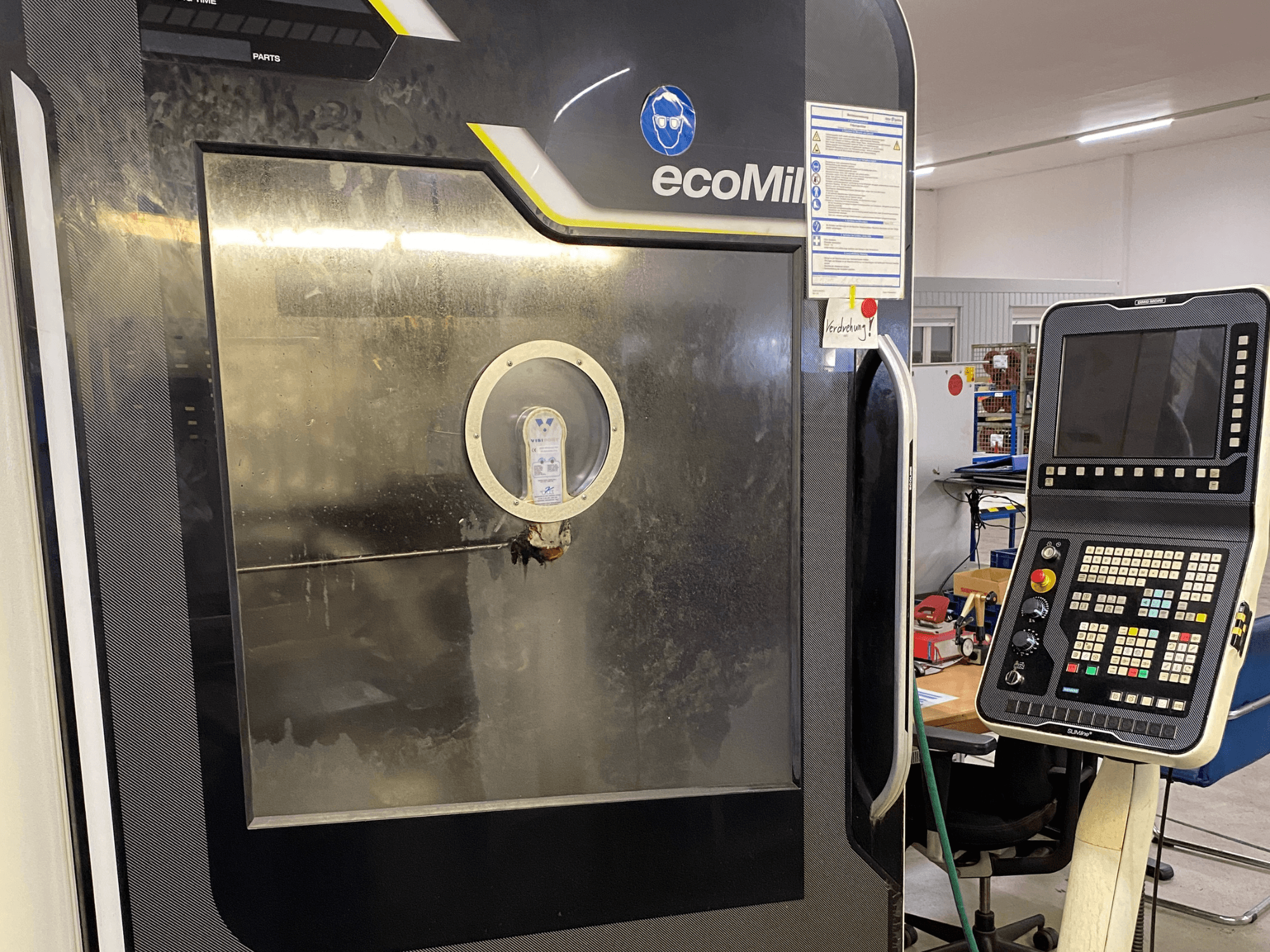 Máquina DMG MU 70 ECO vista de frente, con un panel de control a la derecha y un panel de cristal que permite ver los componentes internos.