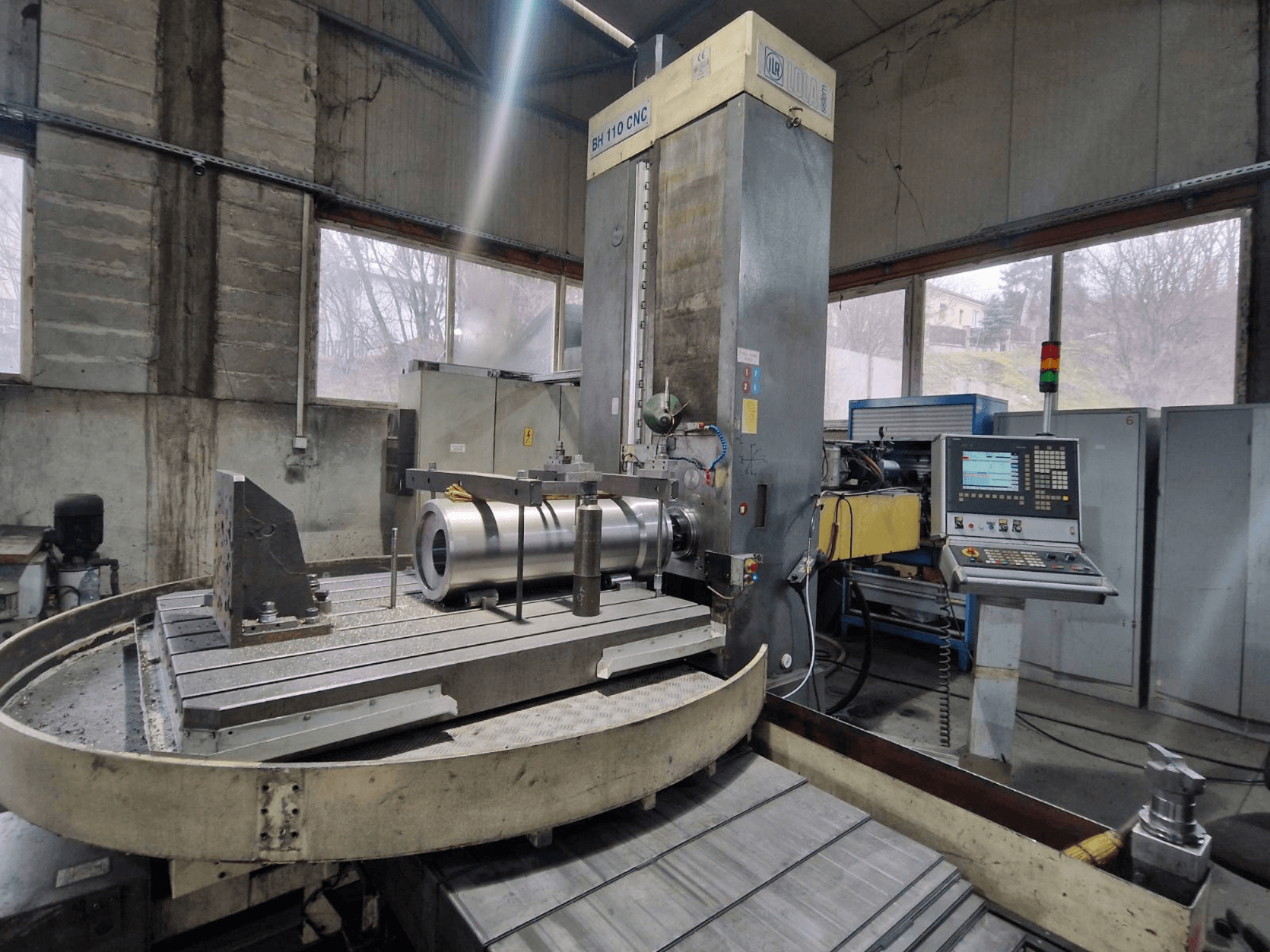 Mandrinadora CNC LOLA BH 110 en un taller, vista frontal, con pieza metálica y panel de control.