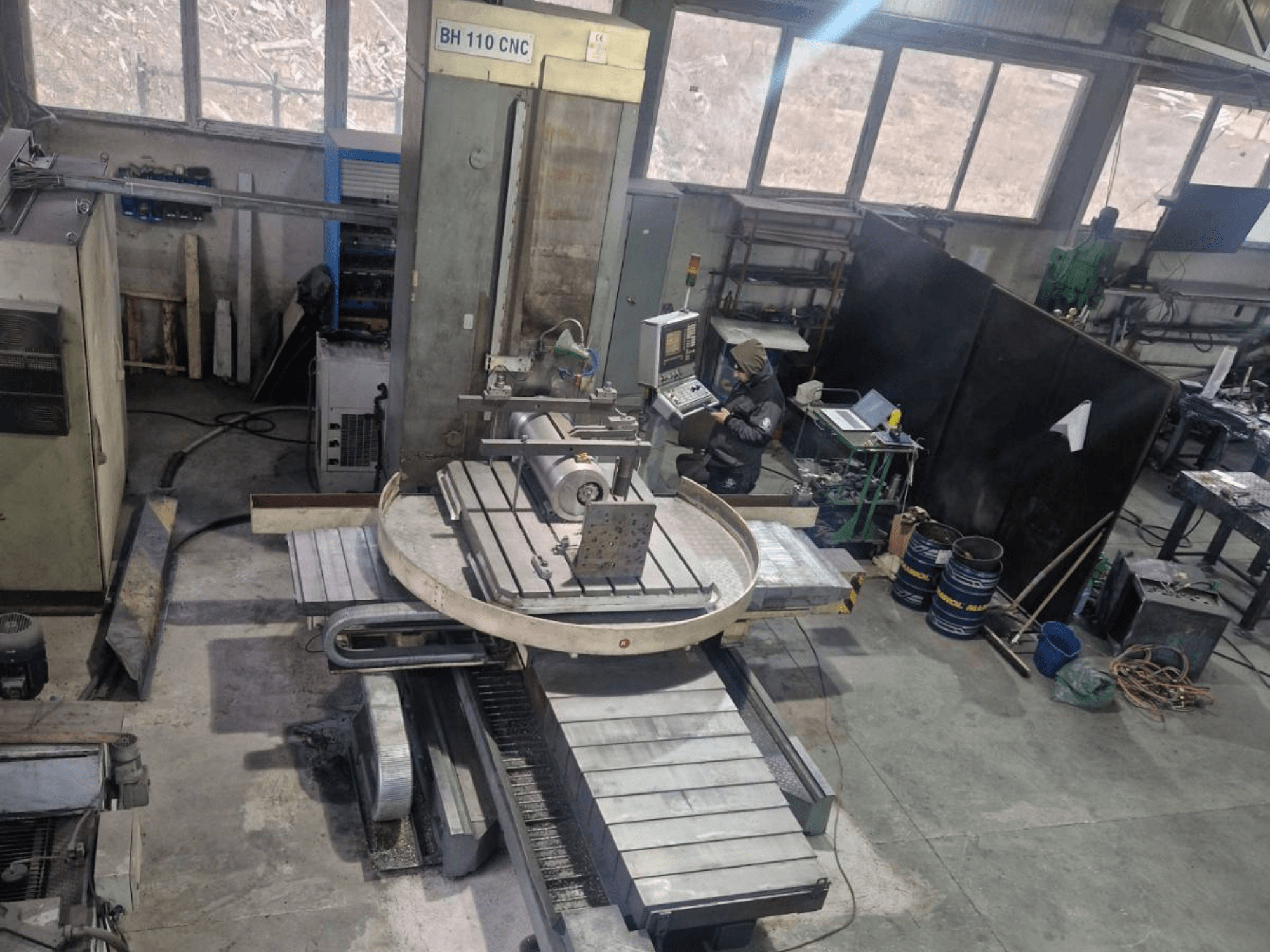 Mandrinadora CNC LOLA BH 110 mostrada desde un ángulo superior, con una mesa circular, controles y una configuración de la pieza de trabajo.