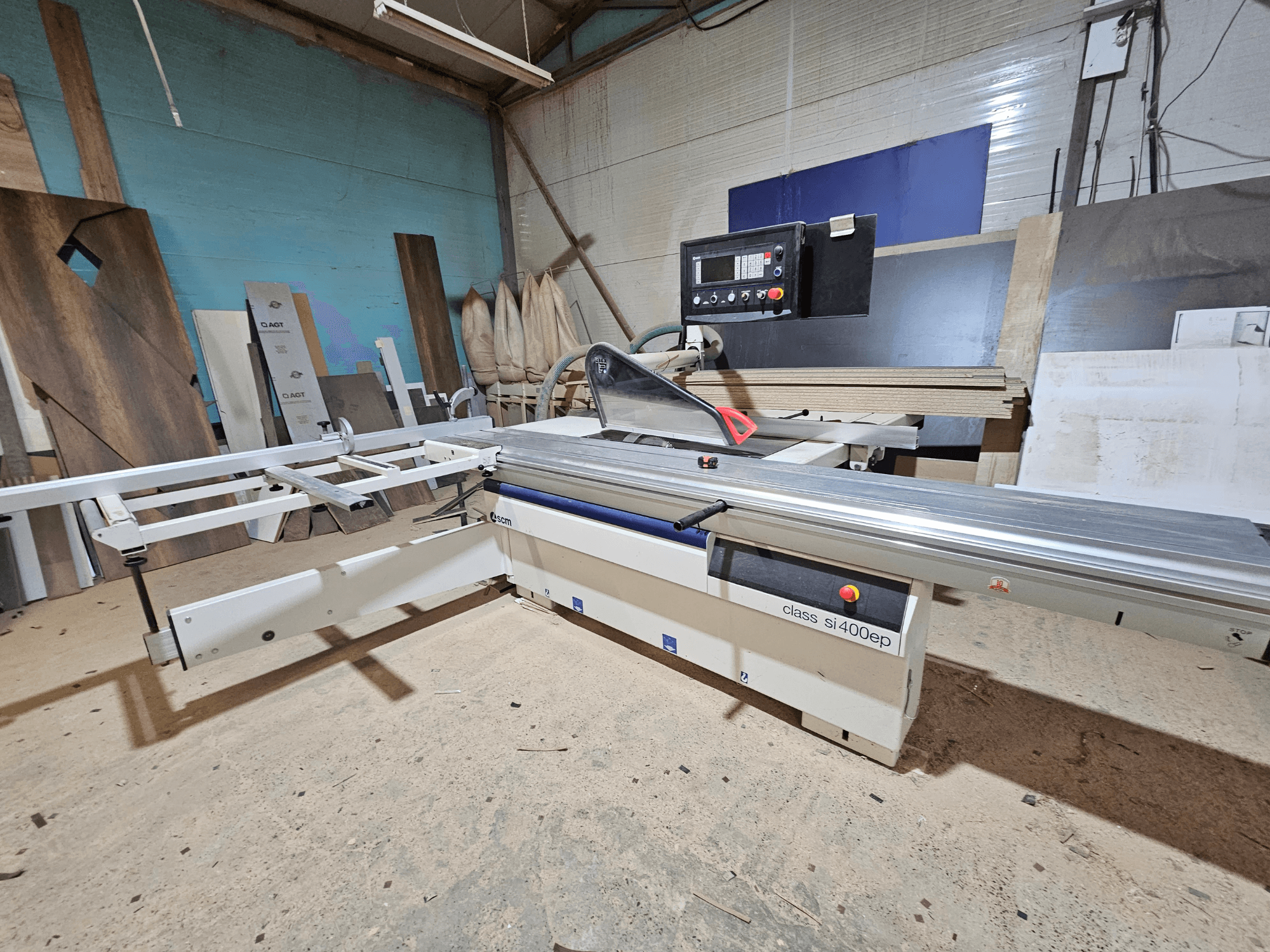 Sierra de paneles de la clase SI400EP, vista frontal, con guía ajustable, colocada en el suelo arenoso del taller, rodeada de paneles de madera.