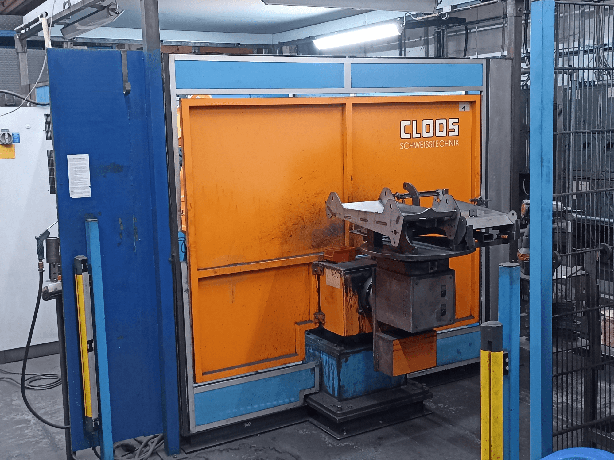Robot de soldadura CLOOS Romat 320 en un taller, vista frontal, con un panel de control naranja y una pieza metálica sobre una base giratoria.