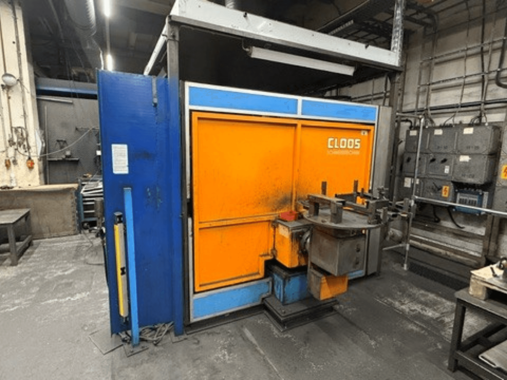 Robot de soldadura CLOOS Romat 320 en un taller; vista frontal en la que se aprecia la cabina de color naranja y azul con el panel de control y las herramientas.