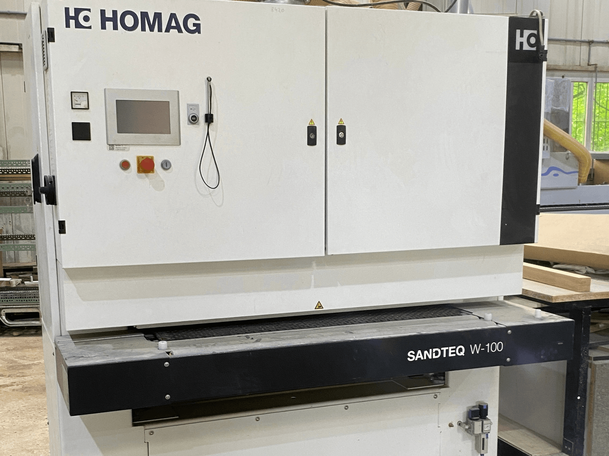 Lijadora de cinta HOMAG SANDTEQ W-100 en un taller, en la que se aprecian el panel de control, la toma de aspiración y la zona de la cinta lijadora. Vista frontal.