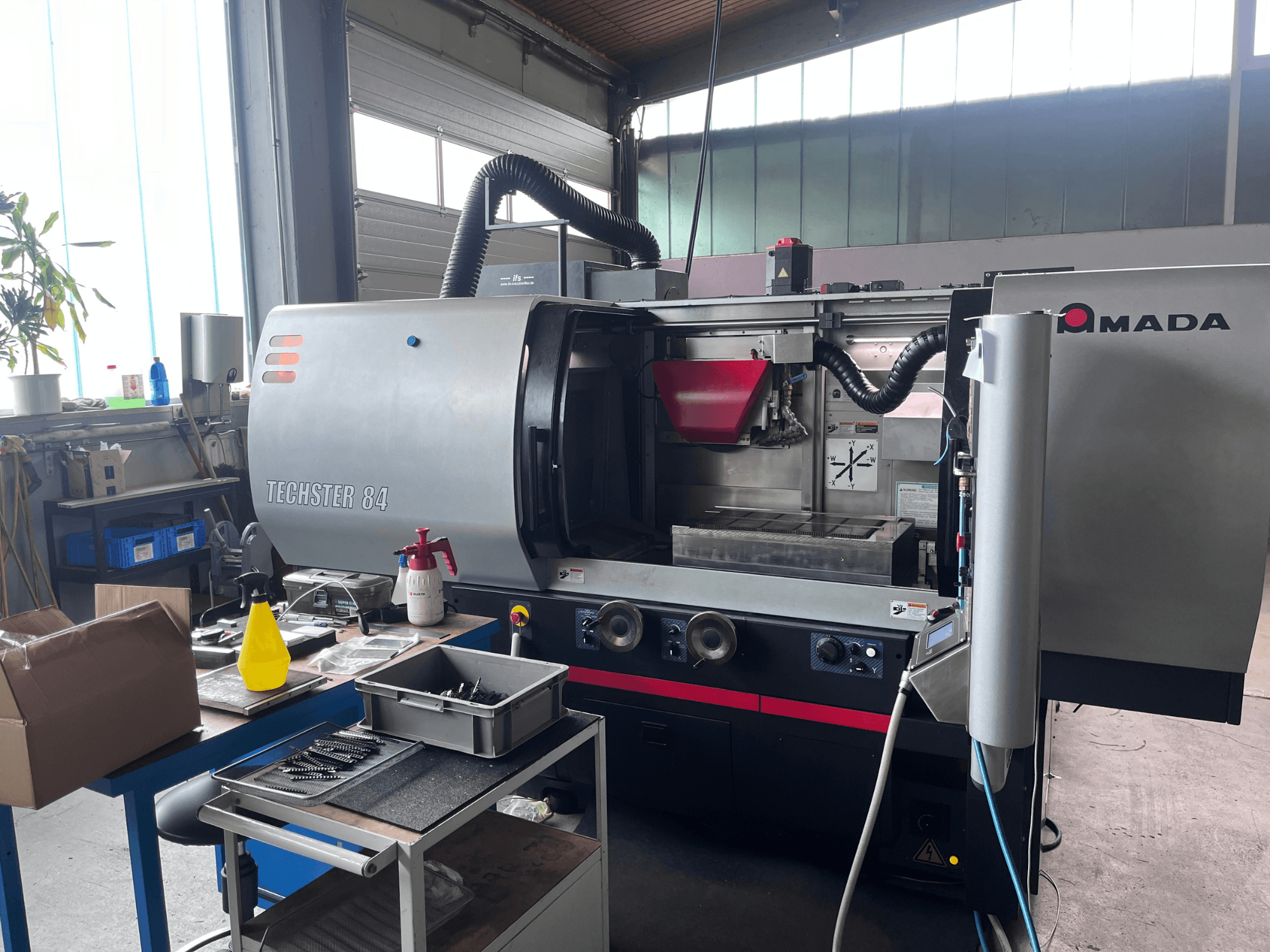 Rectificadora plana AMADA Techster 84 en un taller, en la que se aprecia una vista frontal con los mandos de funcionamiento y la tolva roja.