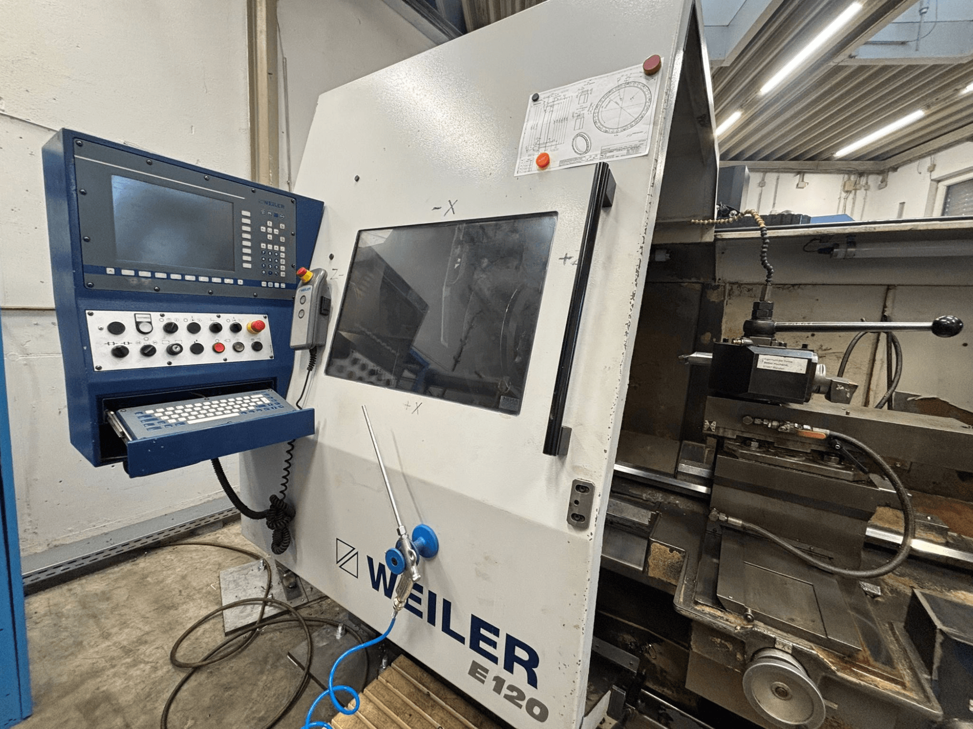 Panel de control e interfaz de la máquina CNC Weiler E-120, vista frontal con botones visibles, pantalla de visualización y componentes operativos.