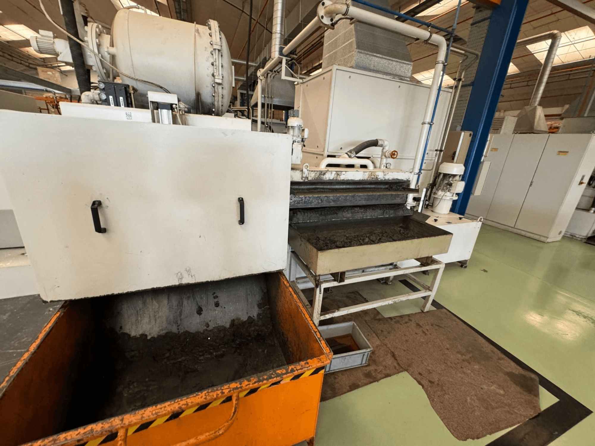 Equipo de procesamiento industrial con un contenedor de residuos naranja, vista frontal; contiene un motor, cintas transportadoras y zona de mantenimiento.