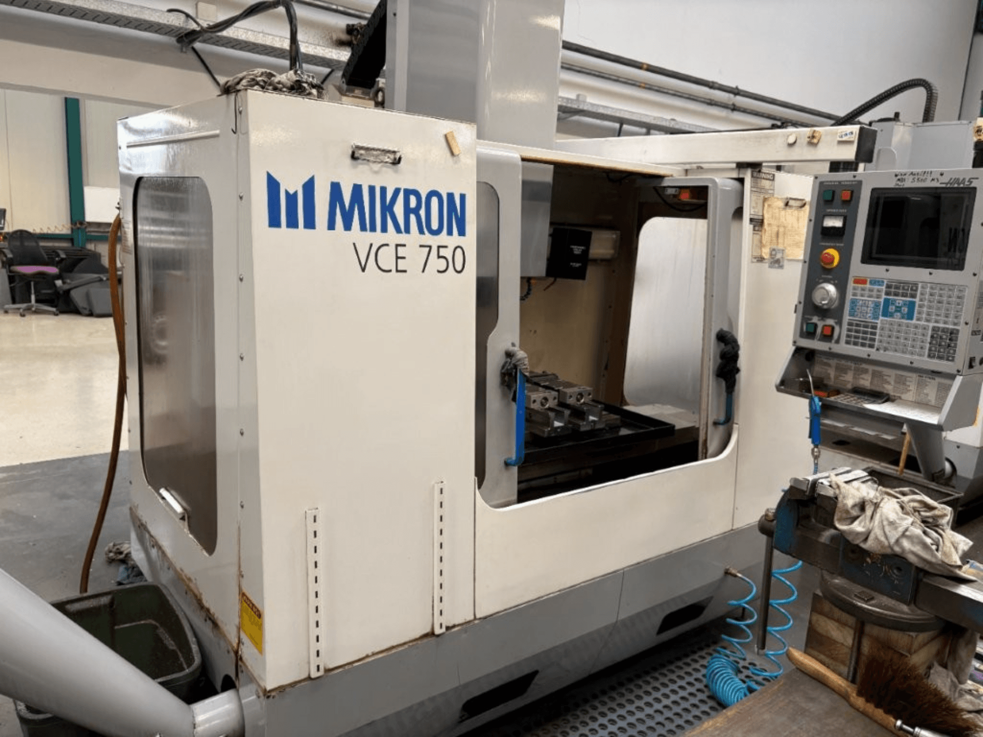 Vista frontal de la fresadora CNC Mikron VCE 750, con mesa de trabajo mecanizada y panel de control con varios botones y pantallas.