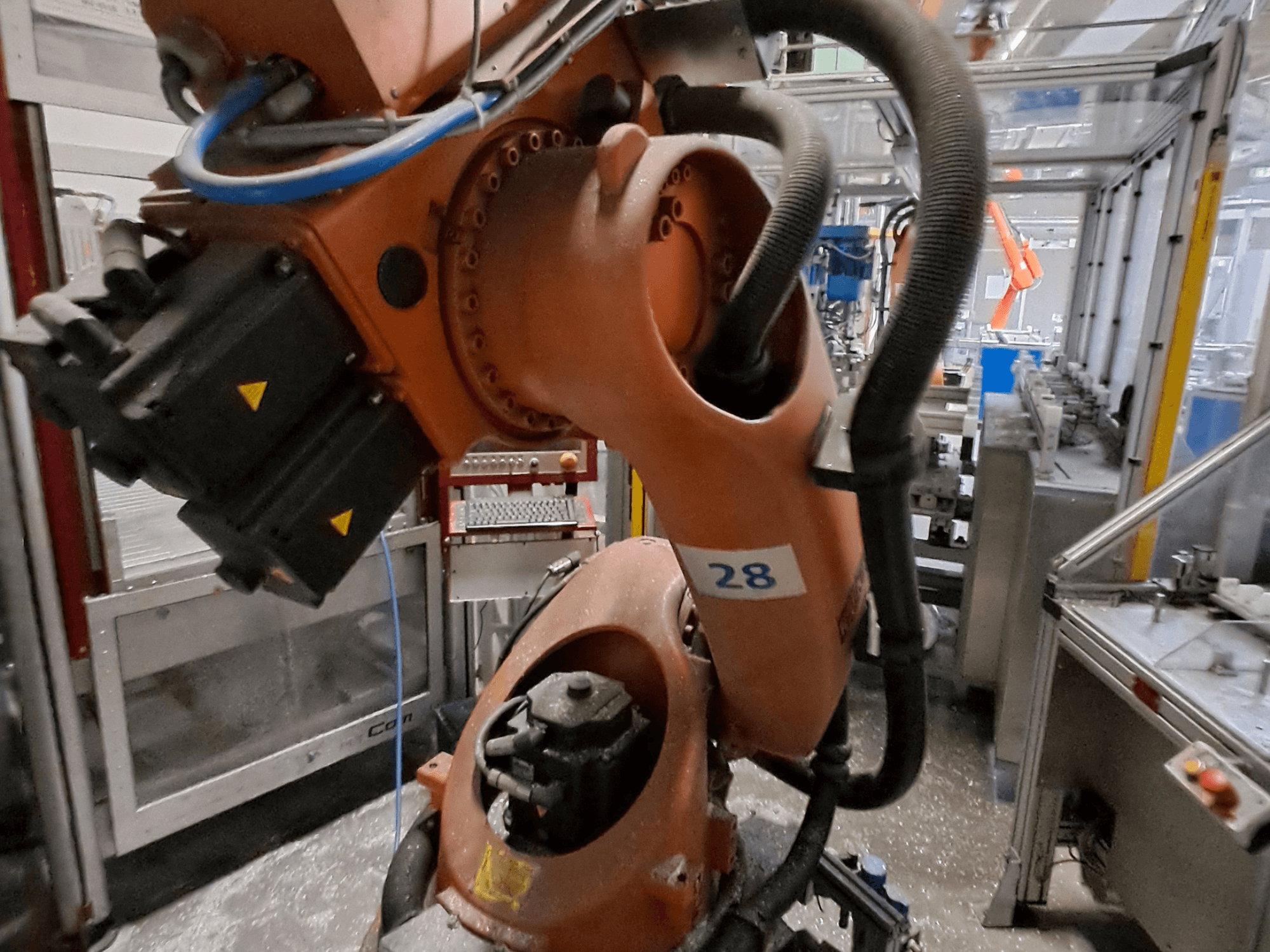 Primer plano del brazo robótico KUKA KR30-3, con el cuerpo de color naranja y la inscripción «28», en el que se aprecian los motores y el cableado desde una vista lateral.