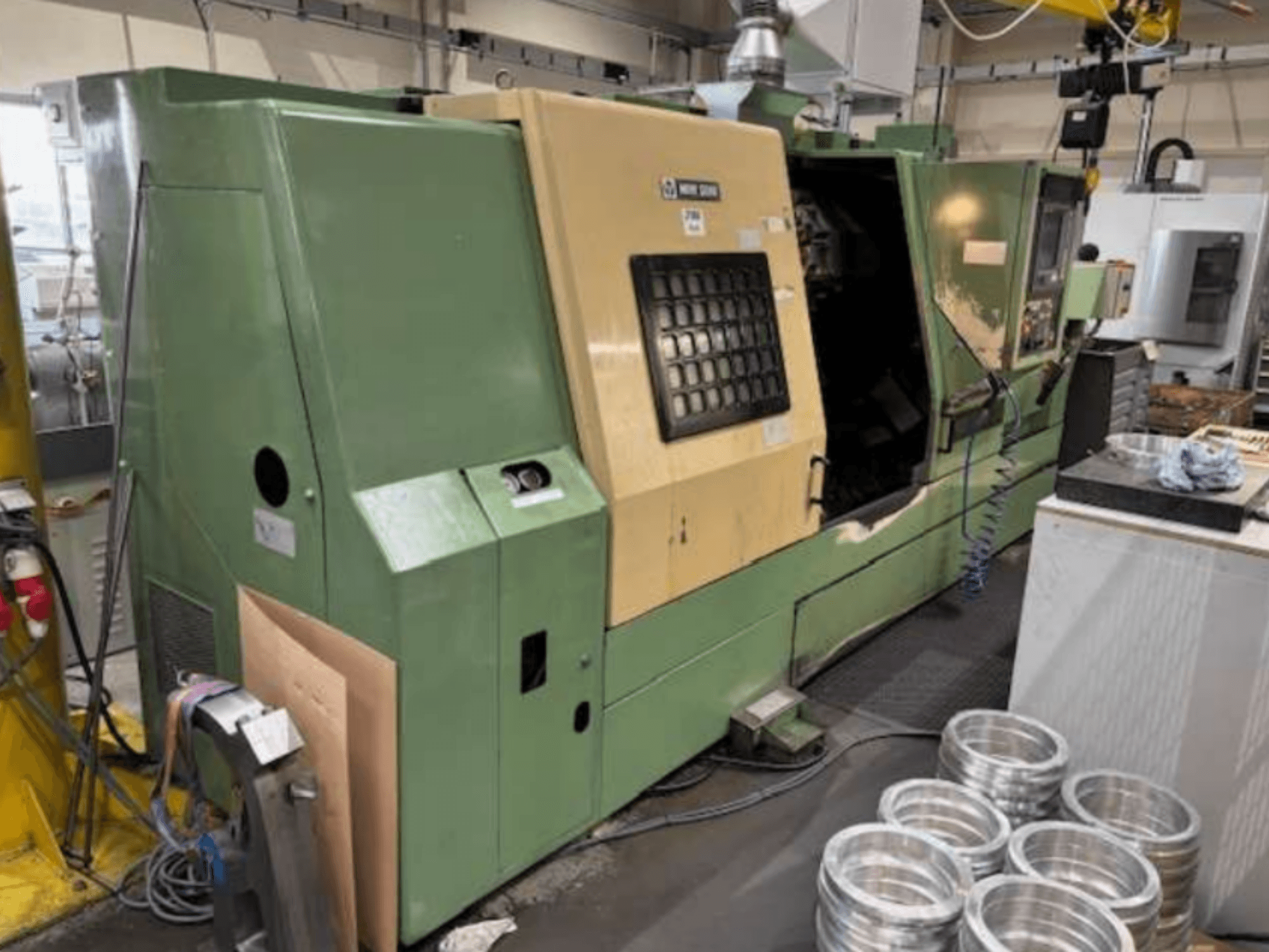 Torno CNC verde de Mazak, visto de frente, mostrando un panel de control y piezas de aluminio mecanizadas sobre una mesa de trabajo.