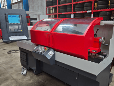 Torno CNC rojo con panel de control, vista frontal; incluye cubierta transparente, portaherramientas y cajones de almacenamiento.