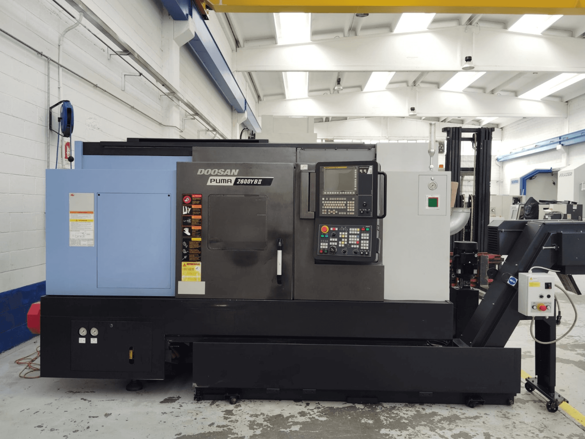 Vista frontal del torno horizontal DOOSAN Puma 2600YB II con el panel de control y las etiquetas de seguridad visibles.