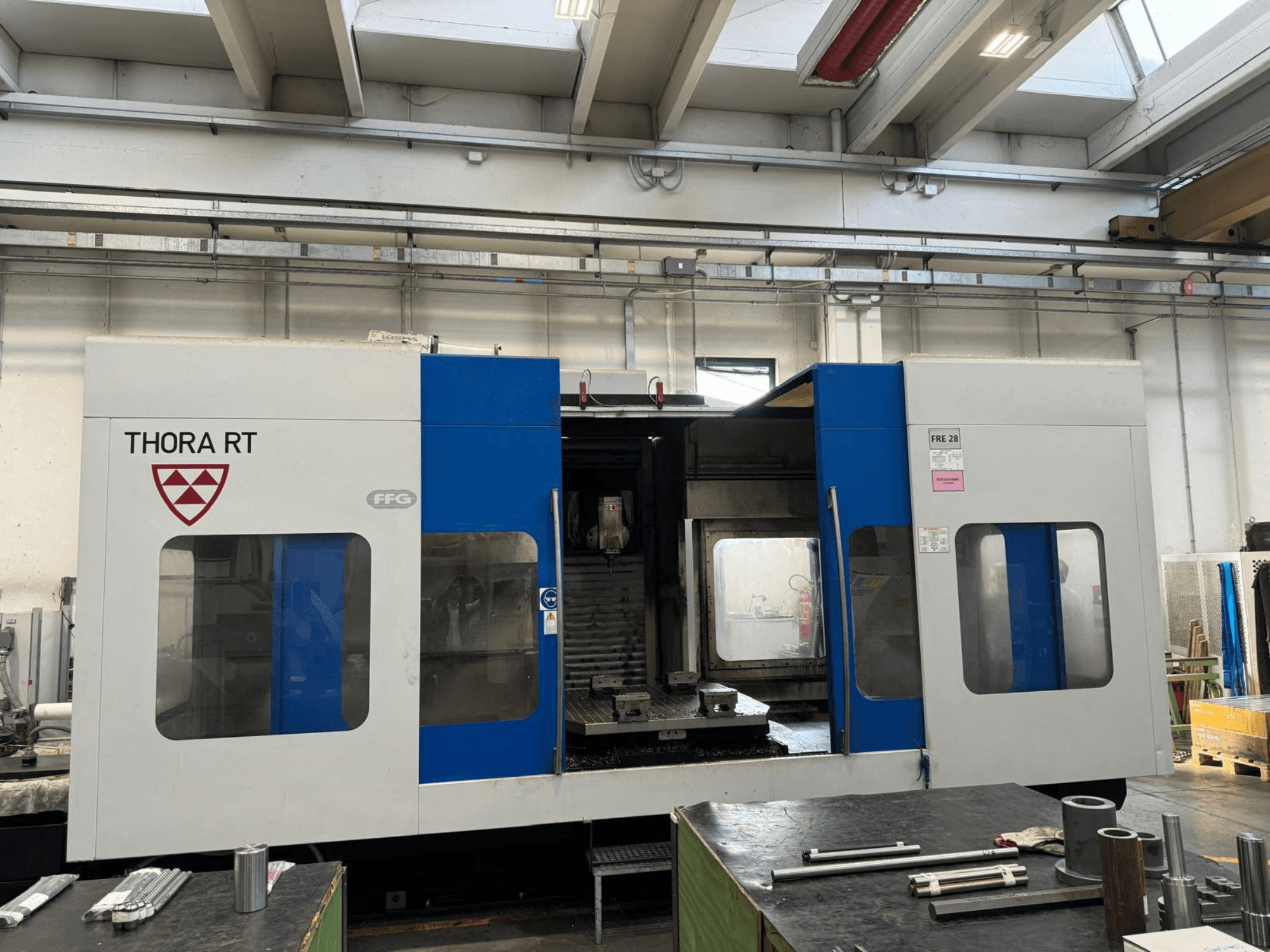 Máquina CNC THORA RT vista de frente, con exterior azul y blanco, ventanas transparentes y herramientas montadas.