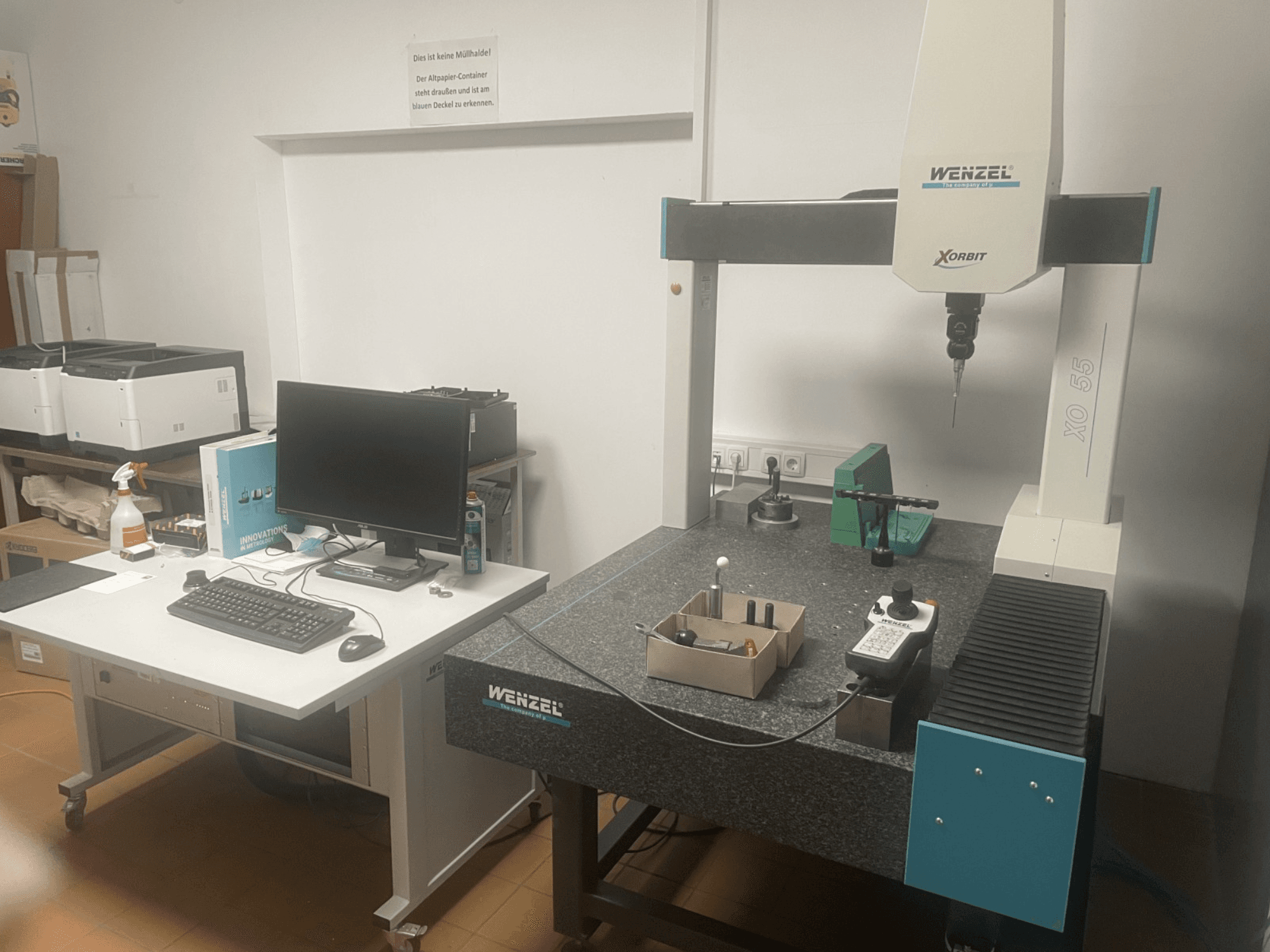 Máquina de medición por coordenadas Wenzel XO 55 con herramientas verdes sobre una mesa de granito, vista de frente con un puesto informático.