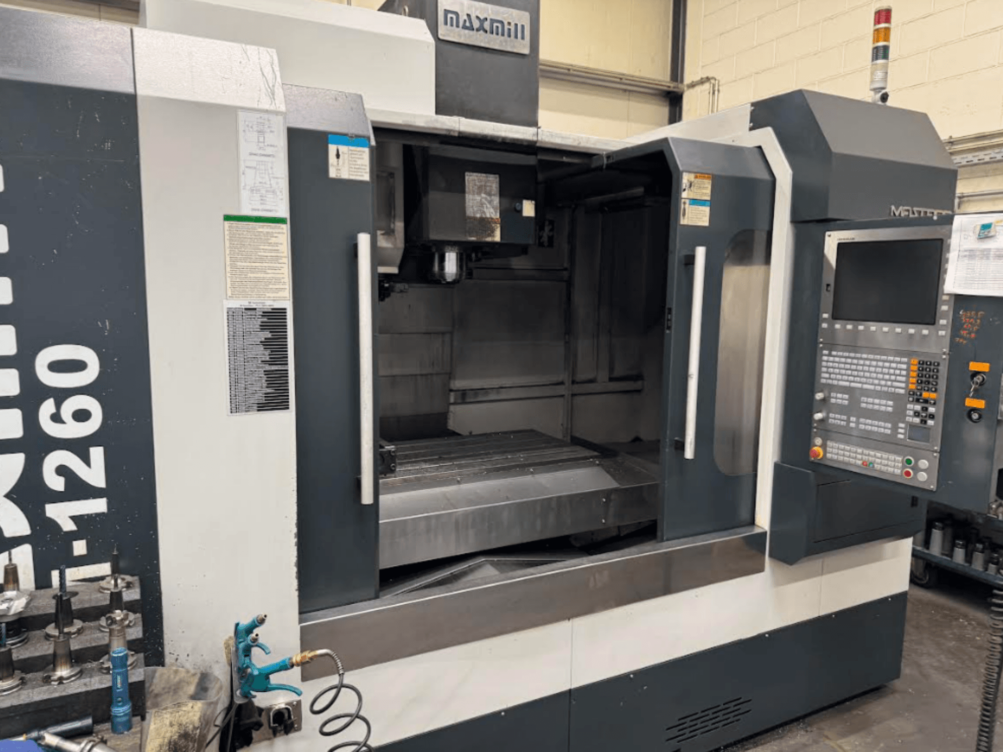 Fresadora CNC Maxmill, modelo M-1260, vista frontal que muestra el espacio de trabajo vacío con el panel de control y las instrucciones de funcionamiento.