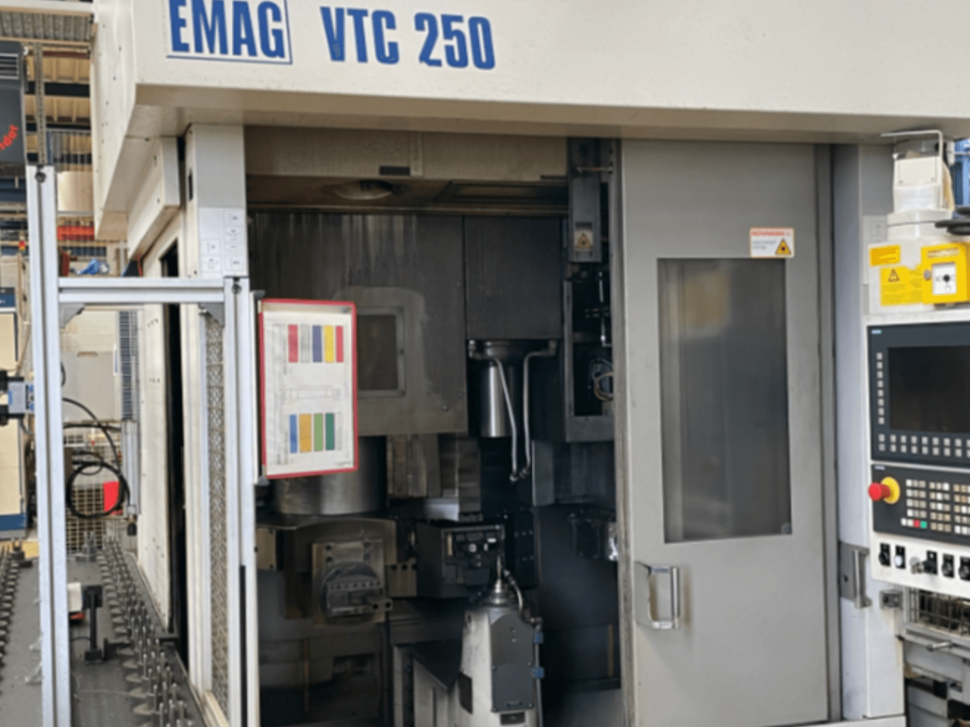 Vista frontal del torno vertical EMAG VTC 250, en la que se aprecian el panel de control, la interfaz operativa y la puerta de acceso abierta.