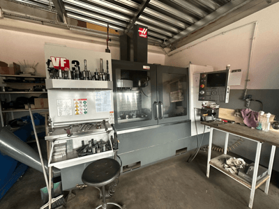 Máquina CNC Haas VF-3 en taller, vista frontal con herramientas y controles en la mesa adyacente, mostrando la interfaz técnica e información de seguridad.