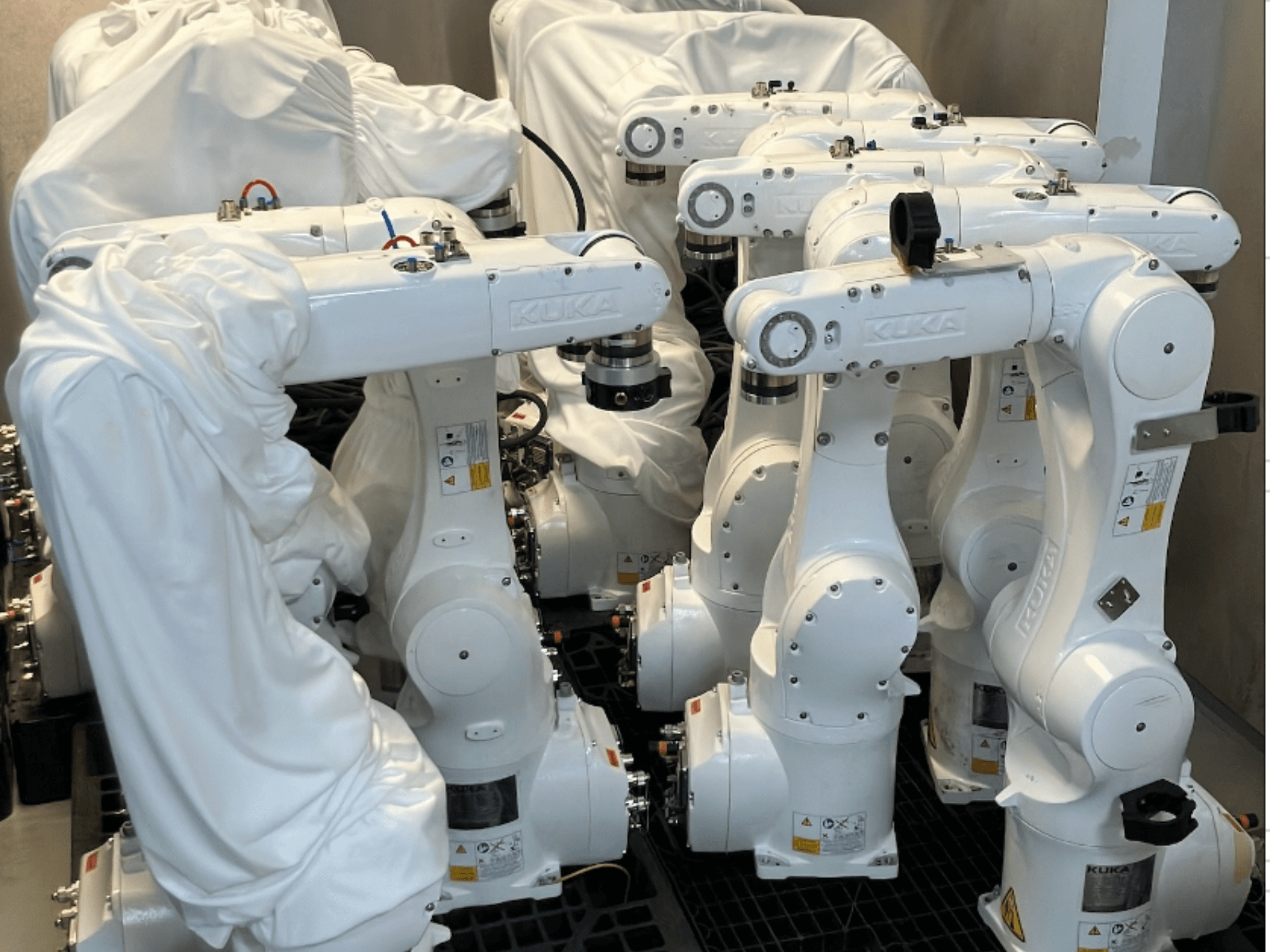 Brazos robóticos KUKA KR 10 R900-2 recubiertos de tela blanca, vistos desde un ángulo superior, mostrando varias unidades almacenadas.