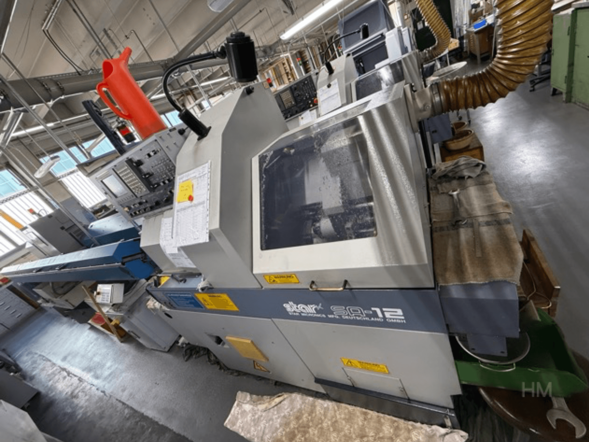 Centro de mecanizado Star SQ-12, vista lateral con panel de control, recipiente de refrigerante y manguera de extracción de polvo visibles.