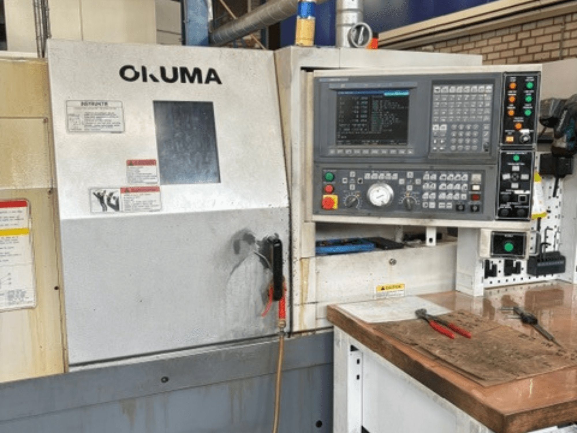 Vista frontal del torno horizontal Okuma ES-L10II, en la que se aprecian el panel de control, la pantalla y el espacio de trabajo con las herramientas.