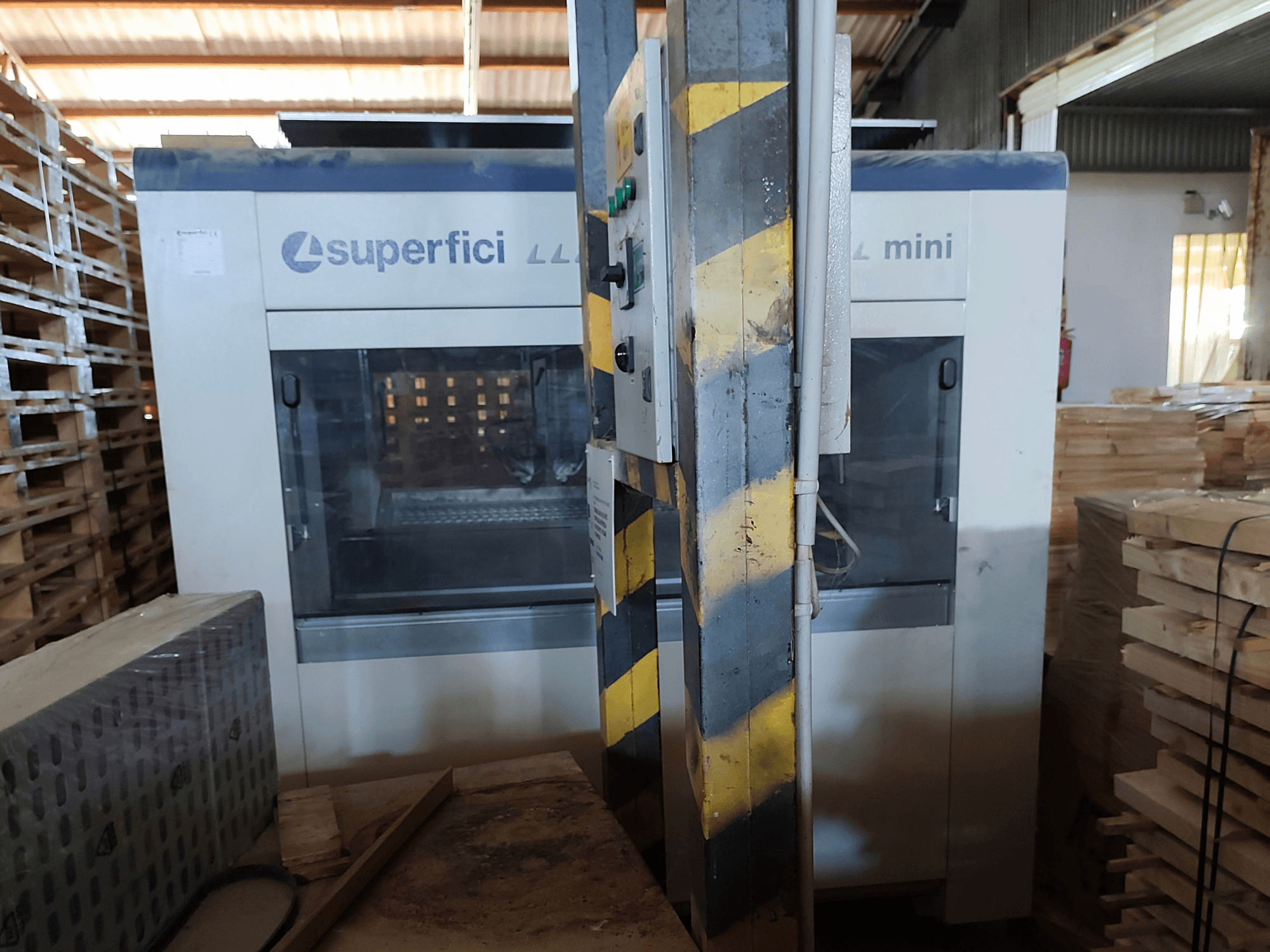 Máquina de acabado de madera SCM Superfici Mini vista de frente, en la que se aprecian el panel de control y los palés de madera que la rodean.