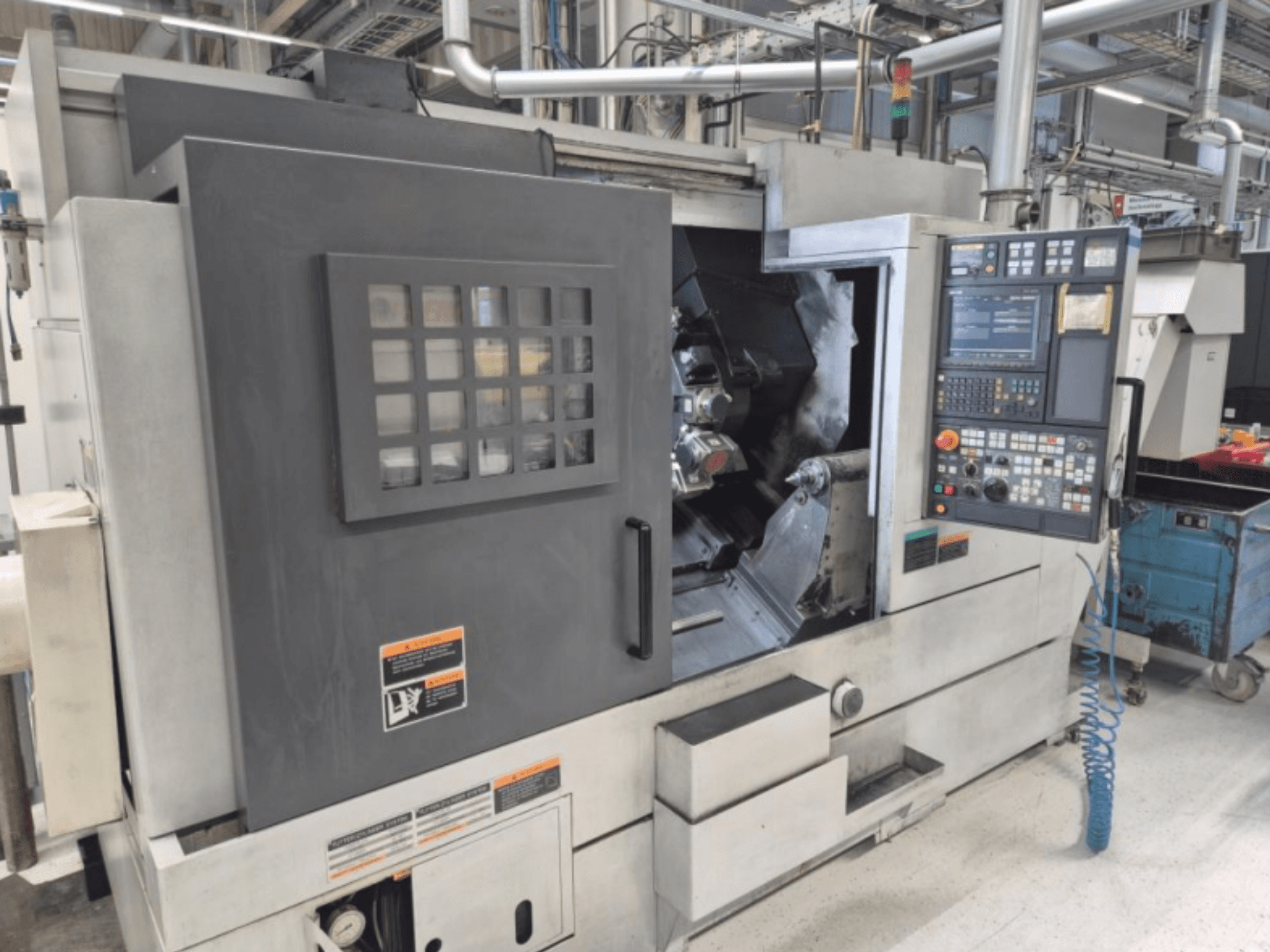 Torno CNC con panel de control, vista frontal. Cuenta con un área de trabajo visible y ventana de seguridad, marca desconocida.