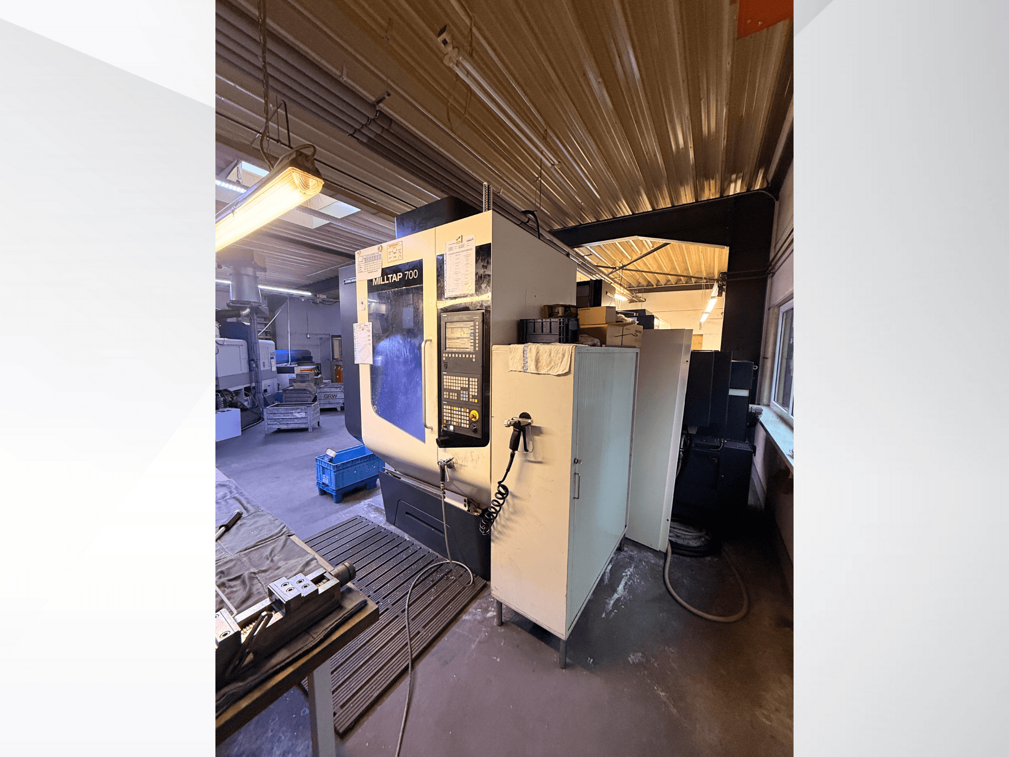 Máquina CNC Milltap 700 en el taller; la vista frontal muestra el panel de control, los estantes para herramientas y las zonas de almacenamiento con iluminación superior.