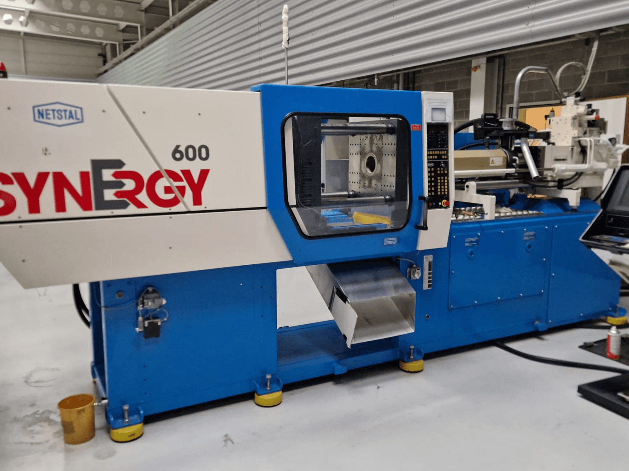 Máquina de moldeo por inyección hidráulica Netstal Synergy 600-230, vista lateral que muestra el panel de control y la zona de inyección.