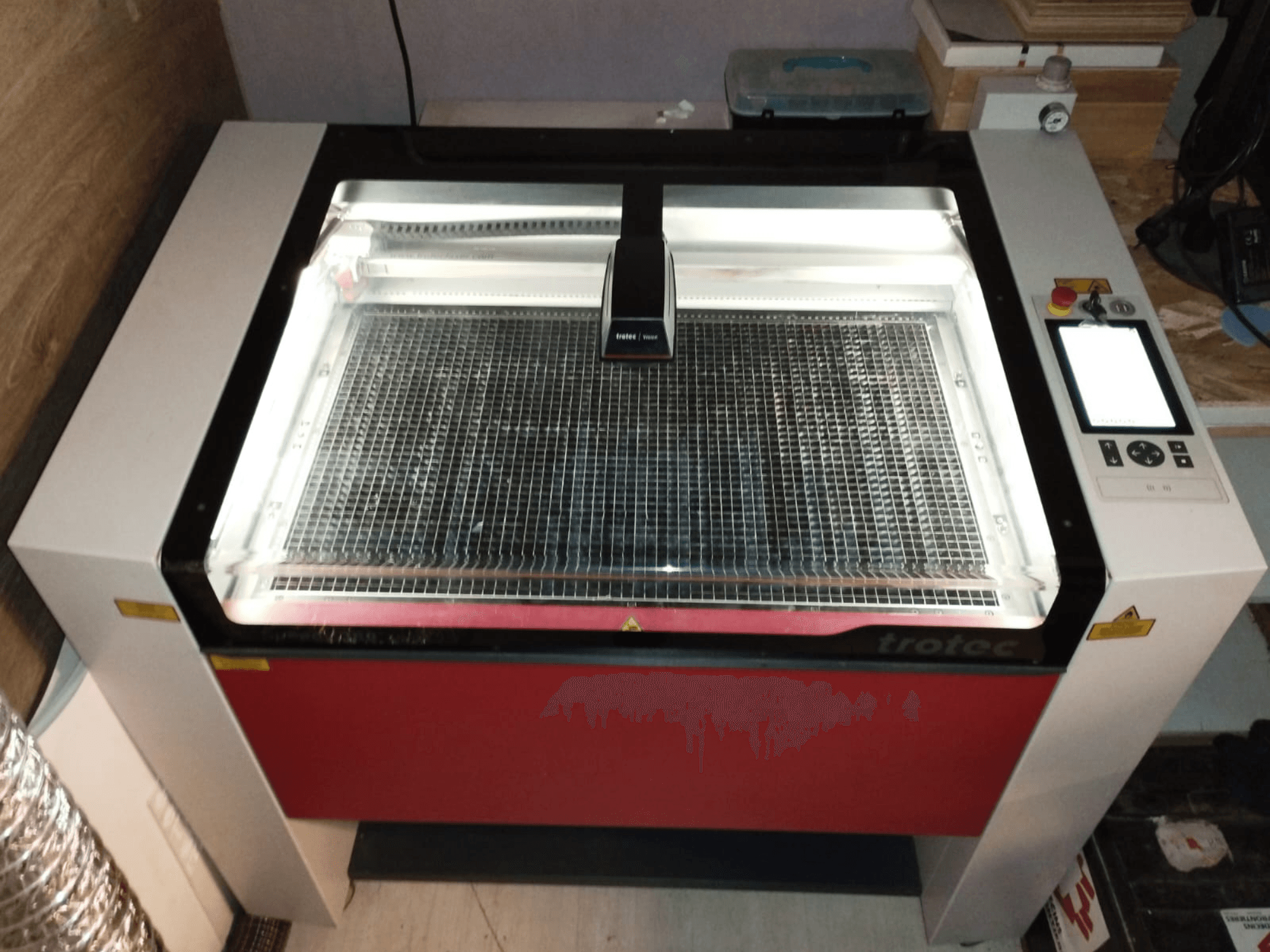Cortadora láser Trotec con tapa transparente, lecho de rejilla y panel de control a la derecha; vista frontal que muestra el diseño y las características.