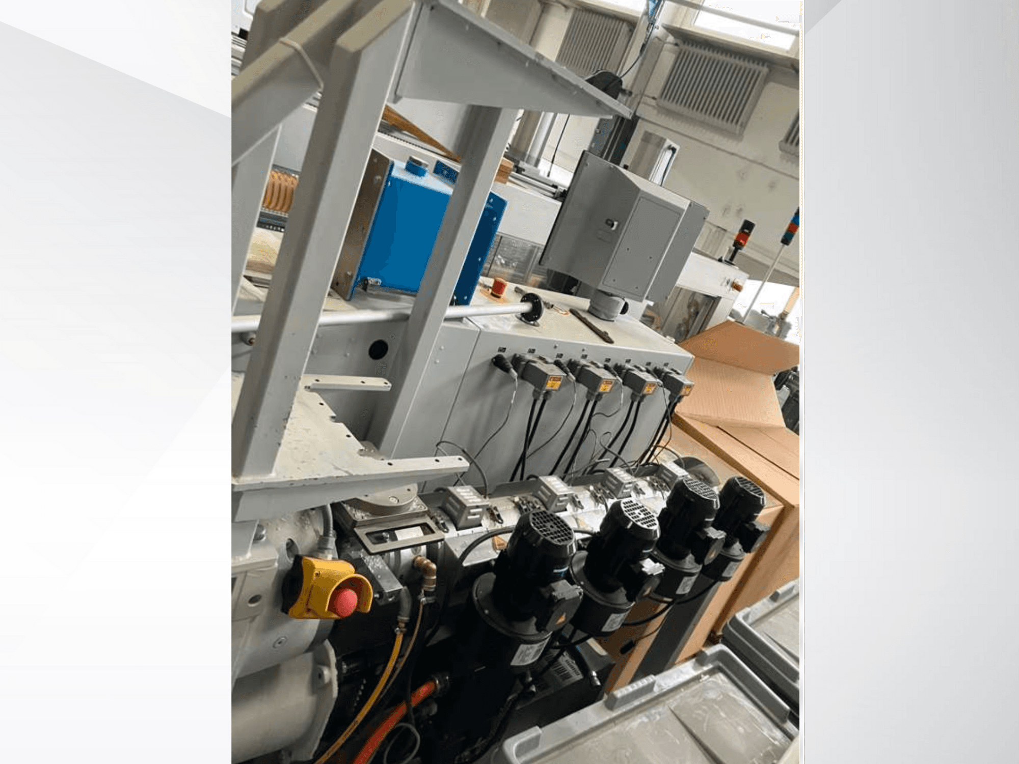 Panel de control de maquinaria industrial con varios motores, indicadores y un monitor; vista lateral en el interior de una fábrica.