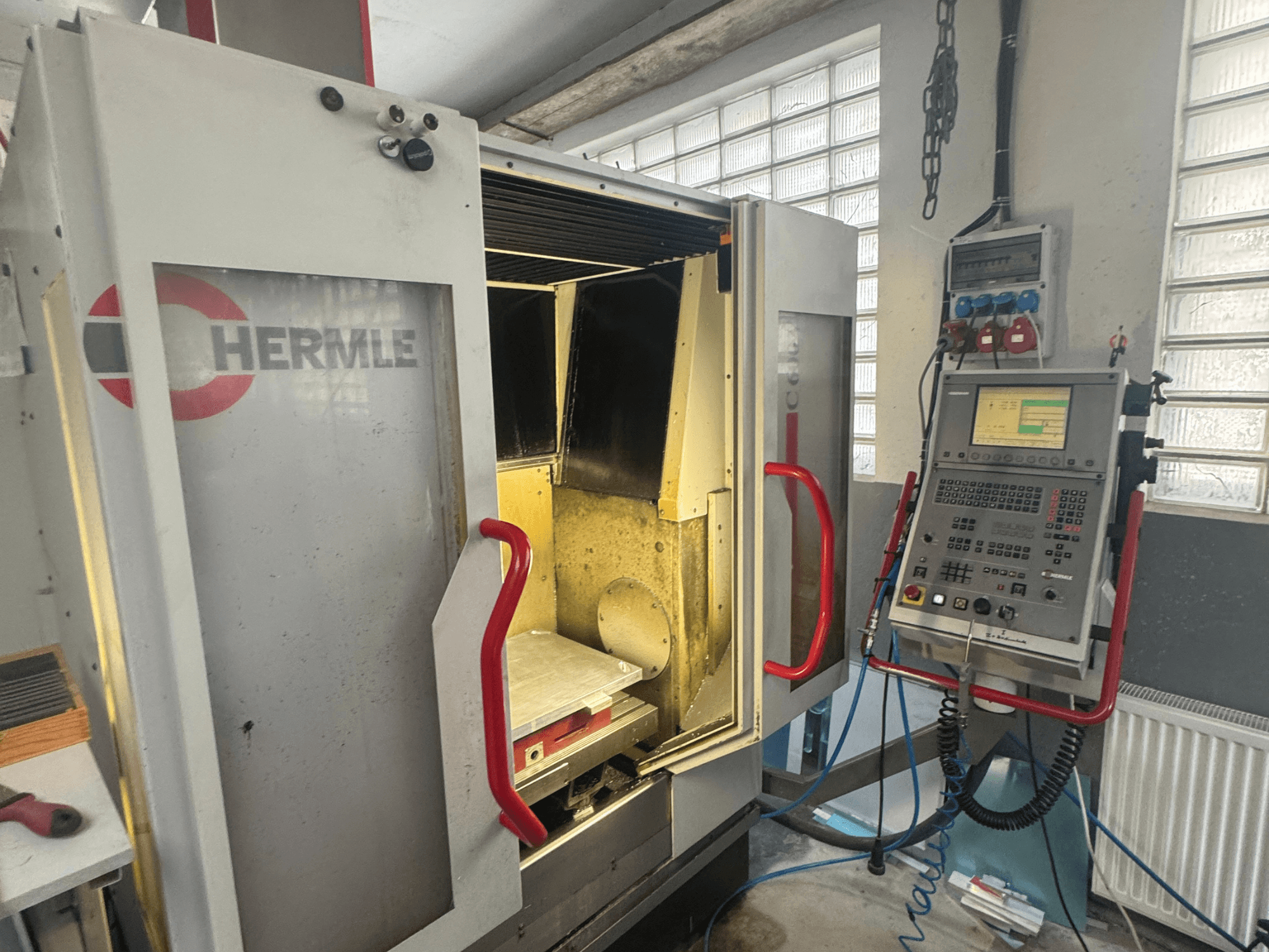 Centro de mecanizado vertical HERMLE C600V, vista frontal mostrando la puerta abierta, el panel de control y el área de trabajo interior.