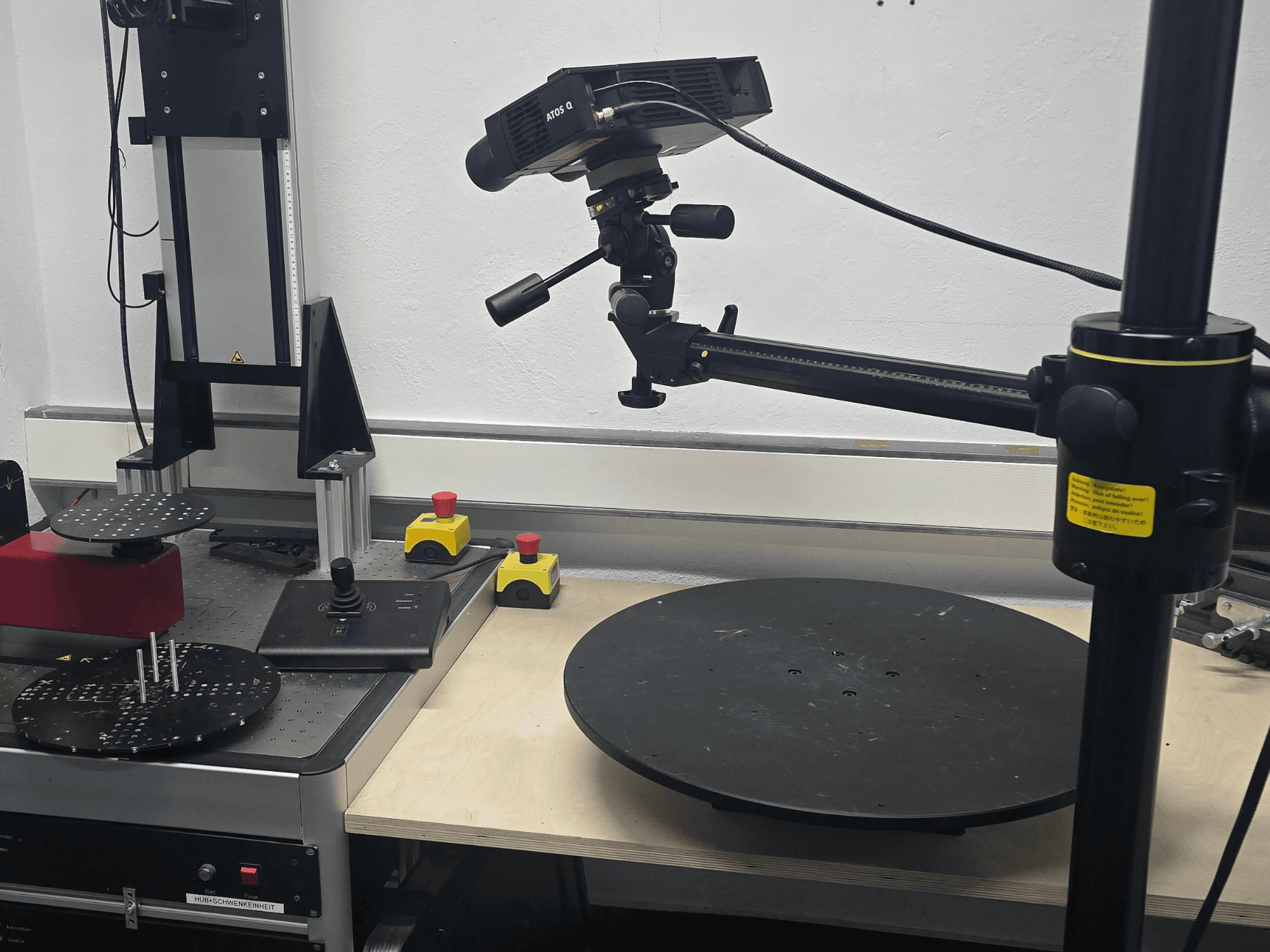 Vista frontal de la máquina de medición óptica ZEISS ATOS Q 12M, que cuenta con un cabezal de escaneo, un panel de control y una plataforma circular giratoria.