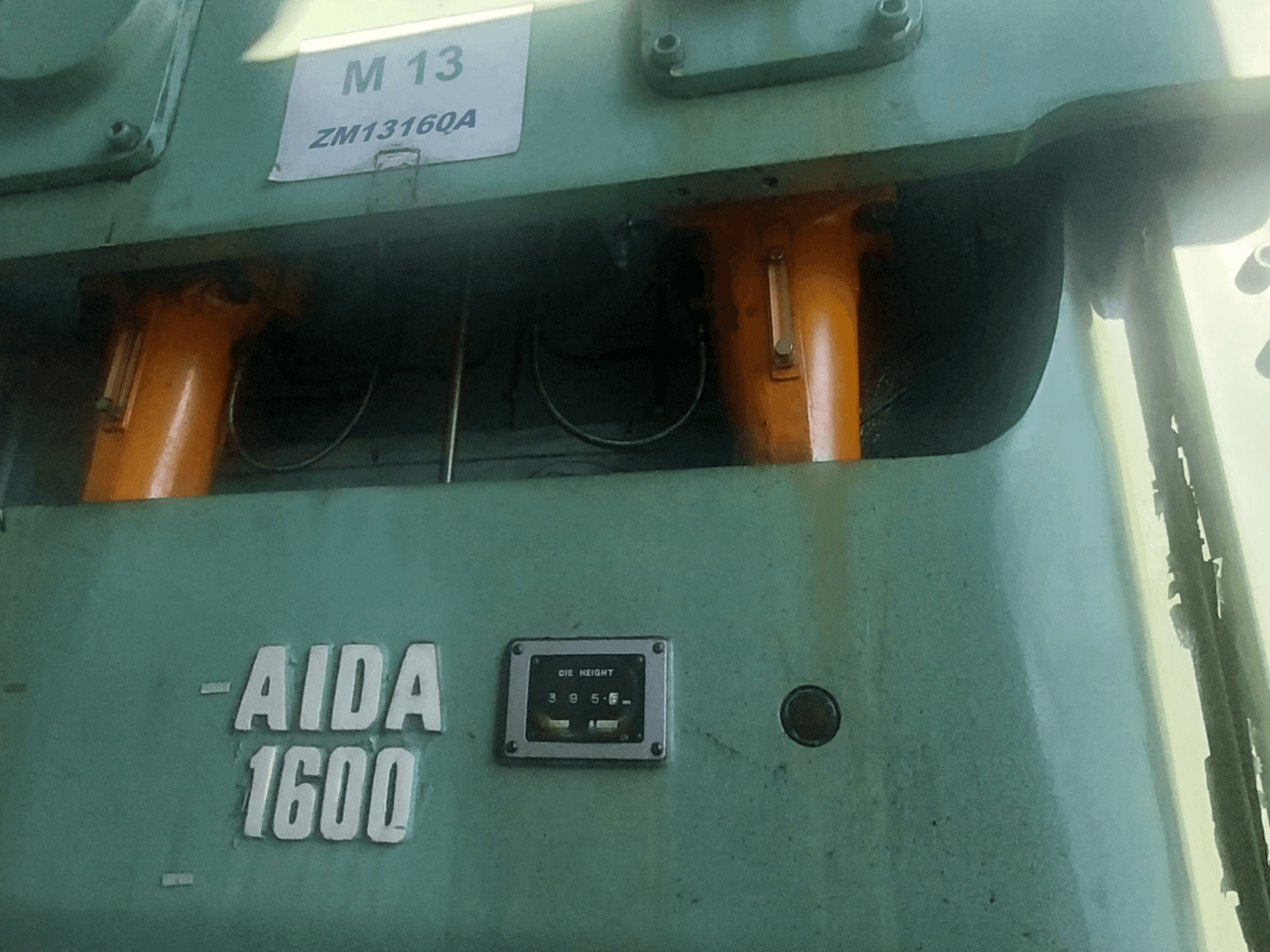 Prensa de estampación mecánica AIDA NC2-1600, vista frontal; componentes hidráulicos naranjas y medidor de altura de troquel visibles.