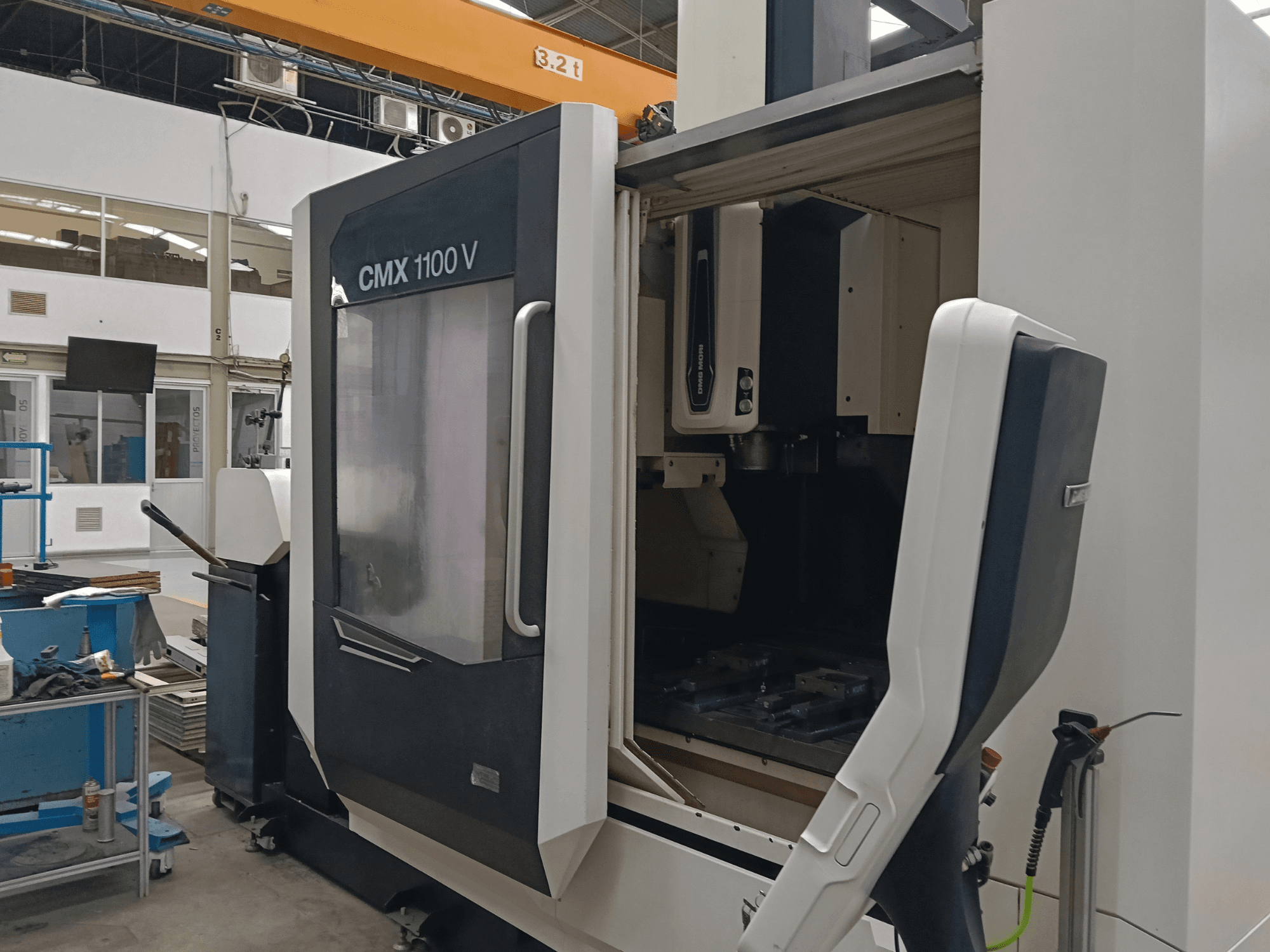 Centro de mecanizado vertical DMG MORI CMX 1100 V; vista frontal que muestra la puerta abierta y la disposición de las herramientas en el interior, en un espacio industrial.
