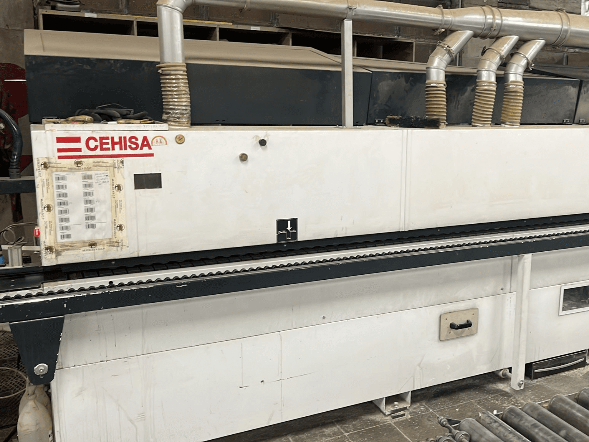La encoladora de cantos CEHISA PRO 12 CONCEPT vista desde delante, en la que se aprecian el panel de control, los tubos de aspiración de polvo y la cinta transportadora.