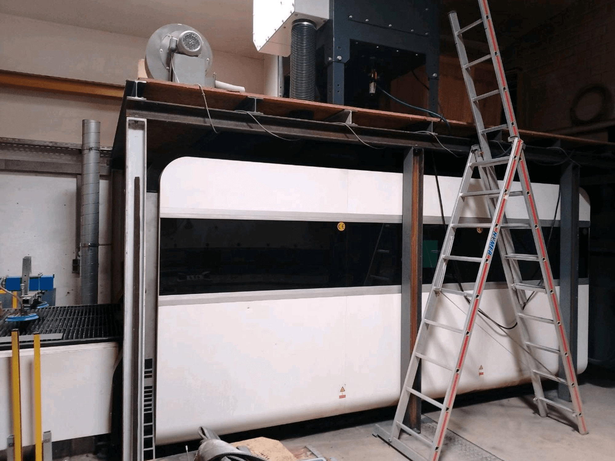 Máquina de corte por láser de fibra GWEIKE LF3015GA en un taller, en la que se aprecia la vista frontal, el bastidor metálico y la escalera de acceso.