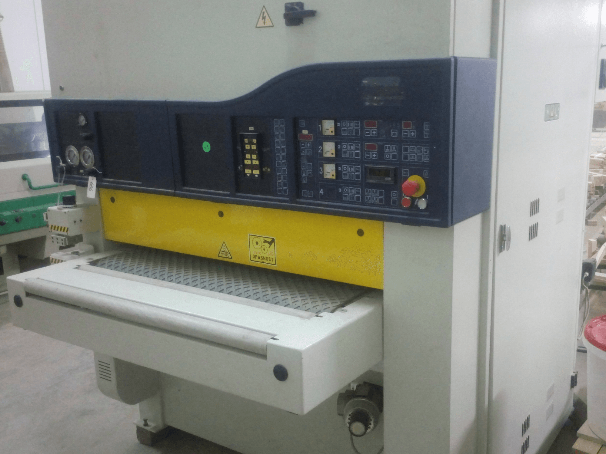 Lijadora industrial con panel de control, cuerpo amarillo y azul, vista frontal, mostrando indicadores, interruptores y superficie de transporte.