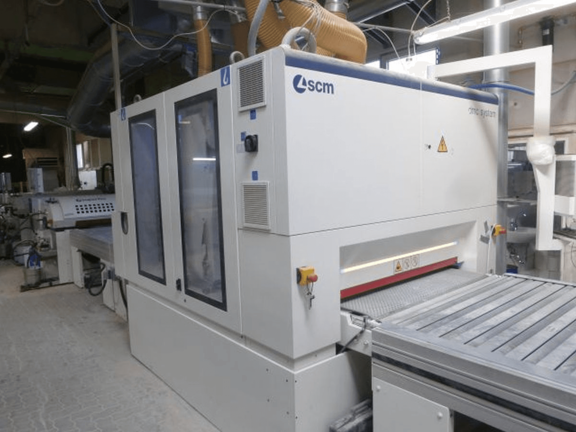 Lijadora de banda SCM DMC SY TC 1350 en un taller; vista lateral en la que se aprecian el panel de control y la superficie de lijado con sus elementos de seguridad.