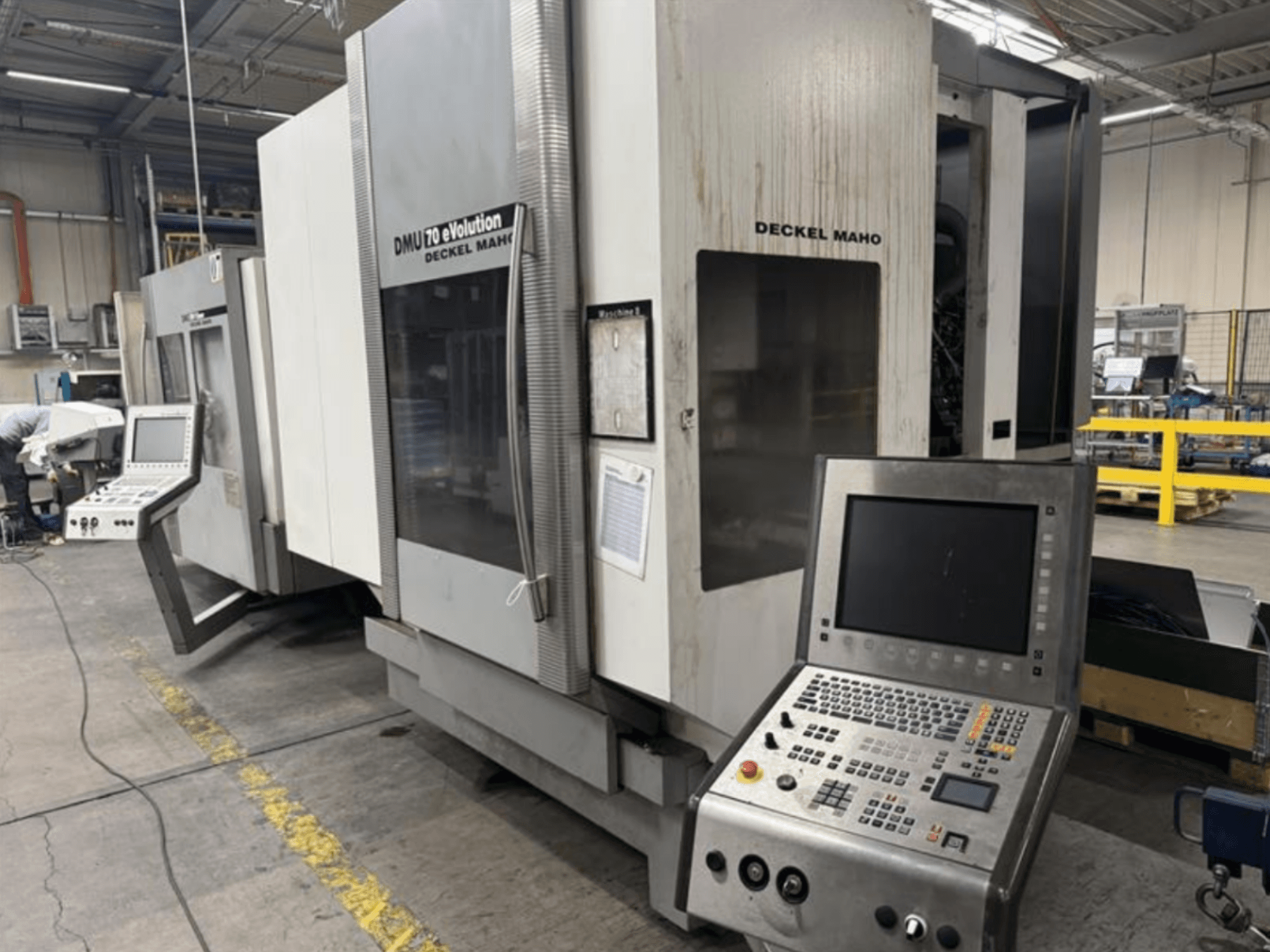 Vista frontal de una máquina CNC Deckel Maho DMU 70 eVOLUTION con panel de control, situada en una planta de fabricación.