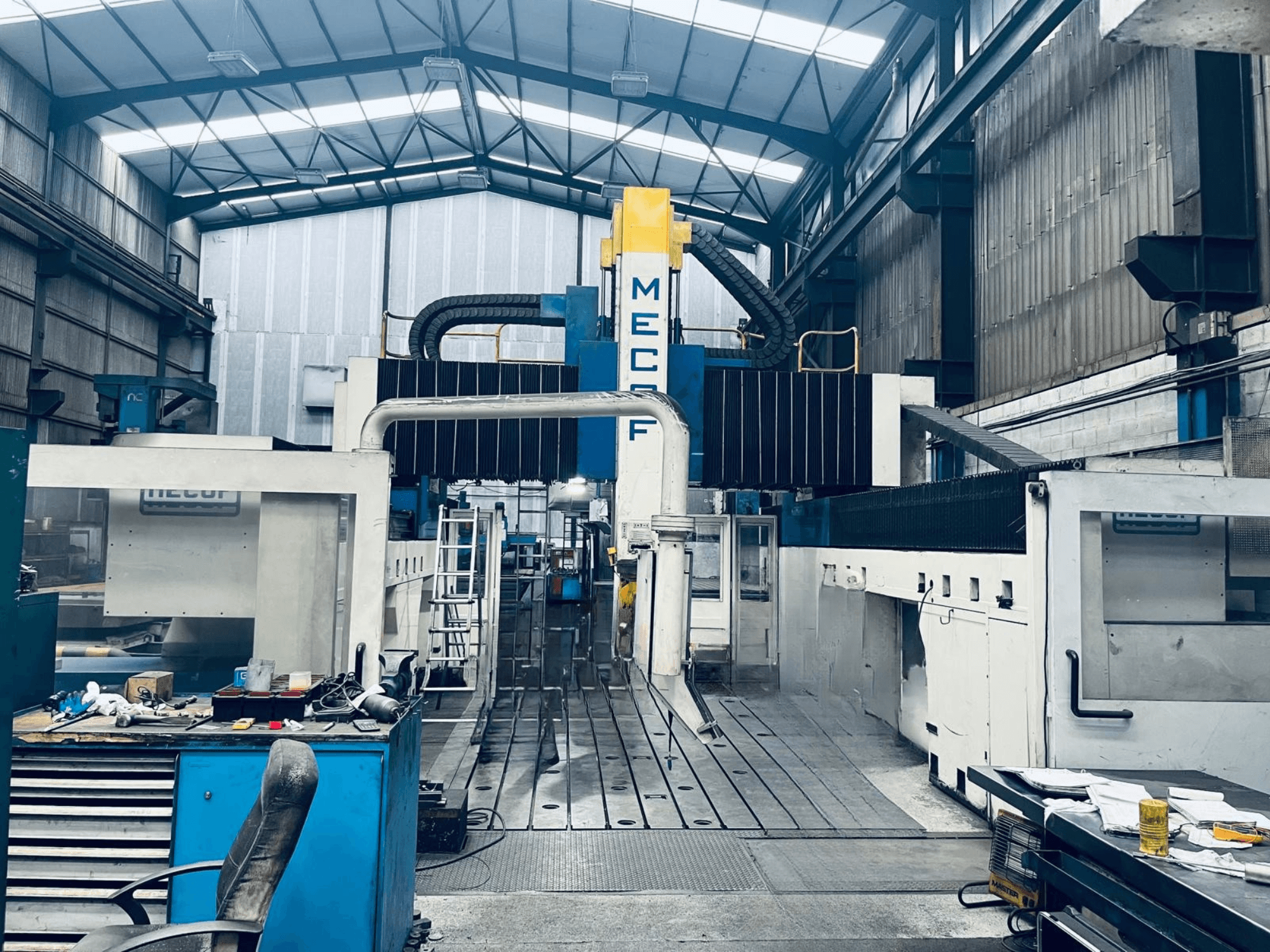 Fresadora de pórtico MECOF DYNAMILL 3000L en el taller, vista frontal, en la que se aprecian la estructura azul y blanca, las herramientas y el espacio de trabajo.