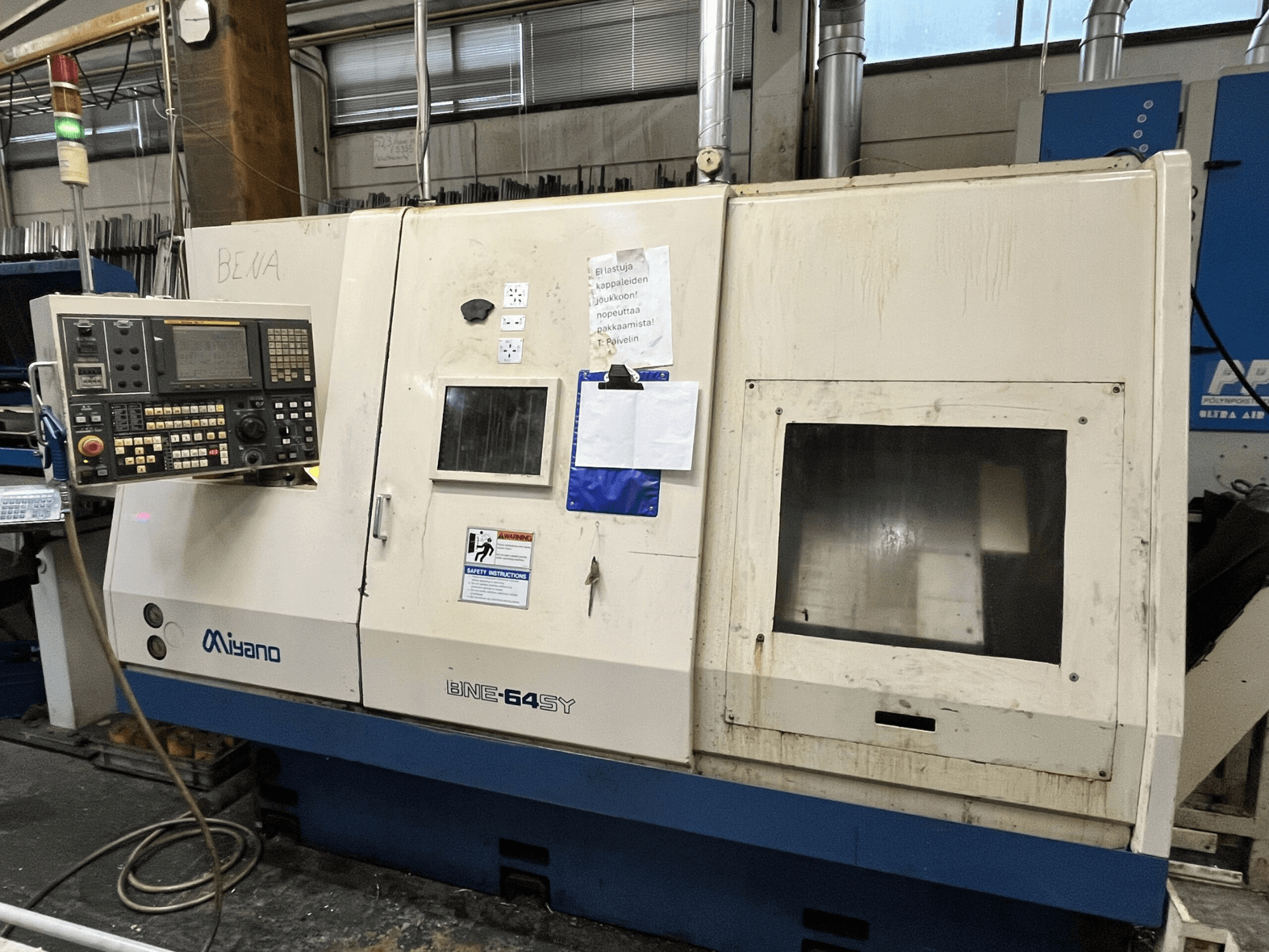 Máquina de torno CNC Miyano BNE-64SY, vista frontal, presenta panel de control con botones, LCD y adhesivos de mantenimiento en el armario.