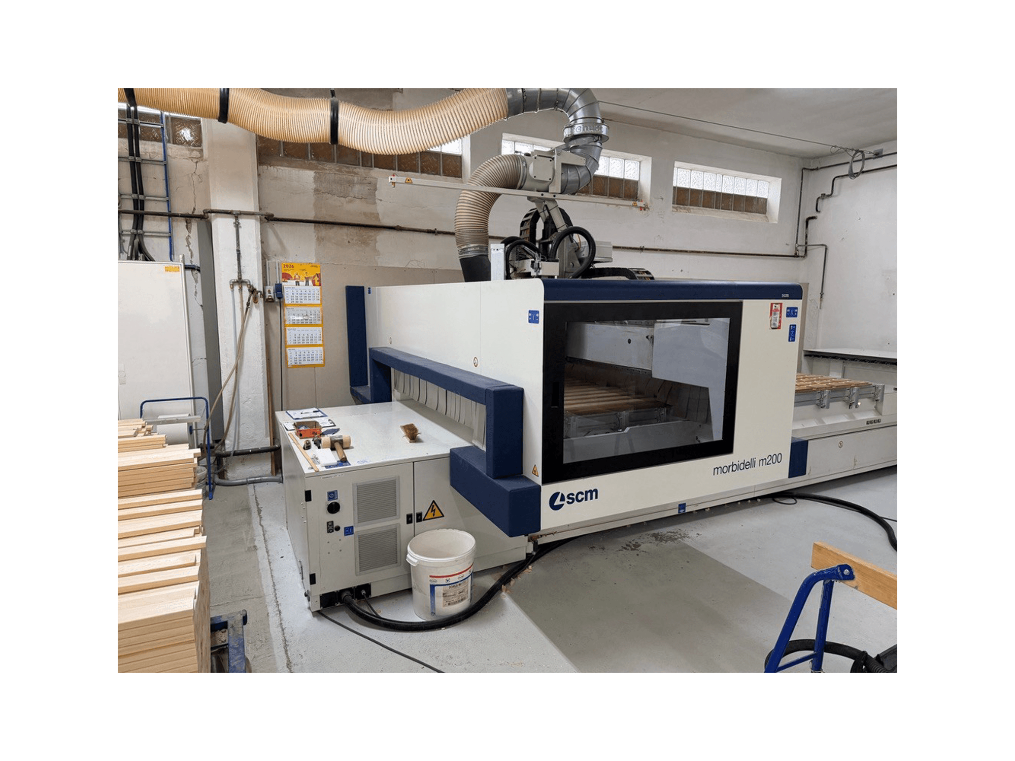 Centro de mecanizado CNC SCM Morbidelli M200F en un taller, vista lateral con piezas de madera sobre la mesa y el sistema de ventilación en la parte superior.