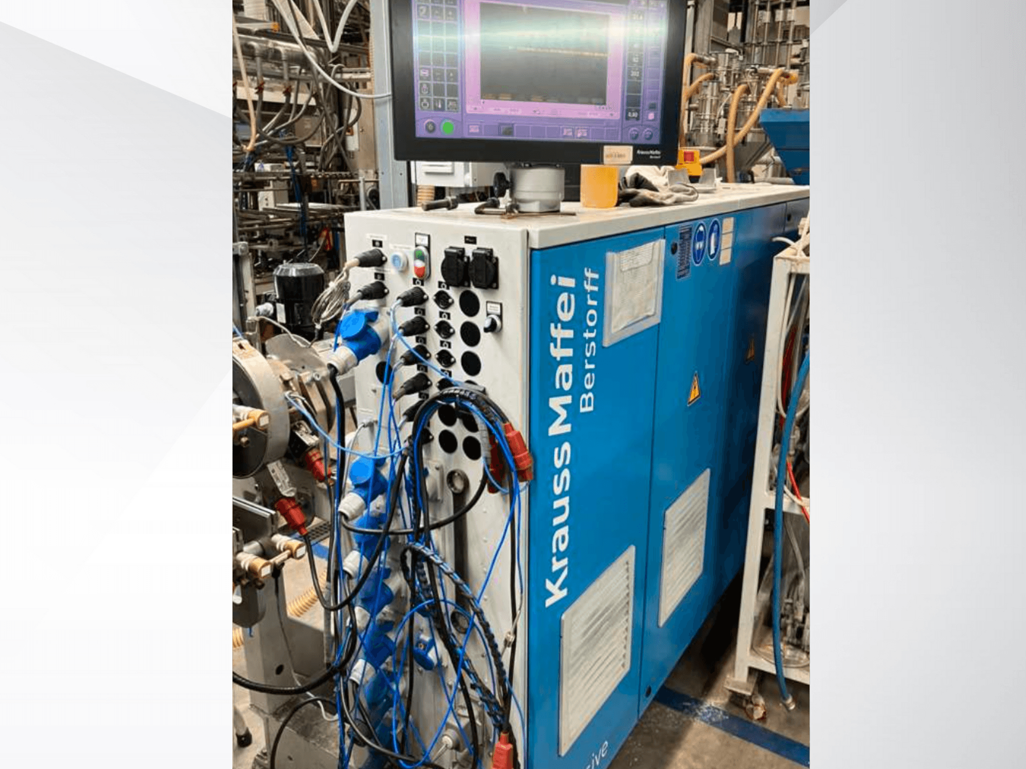 Máquina industrial Krauss Maffei Berstorff con panel de control y monitor, con varios botones y mangueras conectadas, vista lateral.