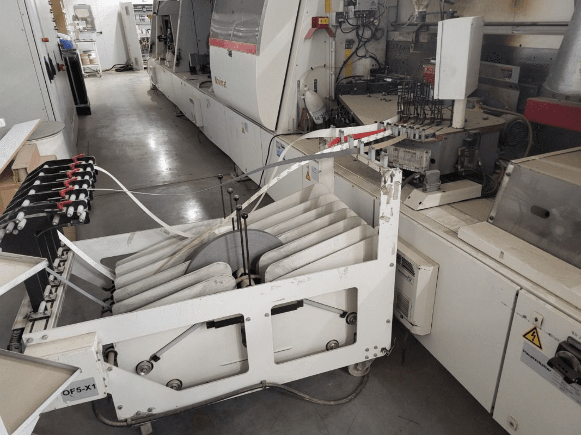Chapadora de cantos IMA Novimat/I/680/650/R3, vista lateral mostrando los rodillos de alimentación y el panel de control en medio del entorno del taller.
