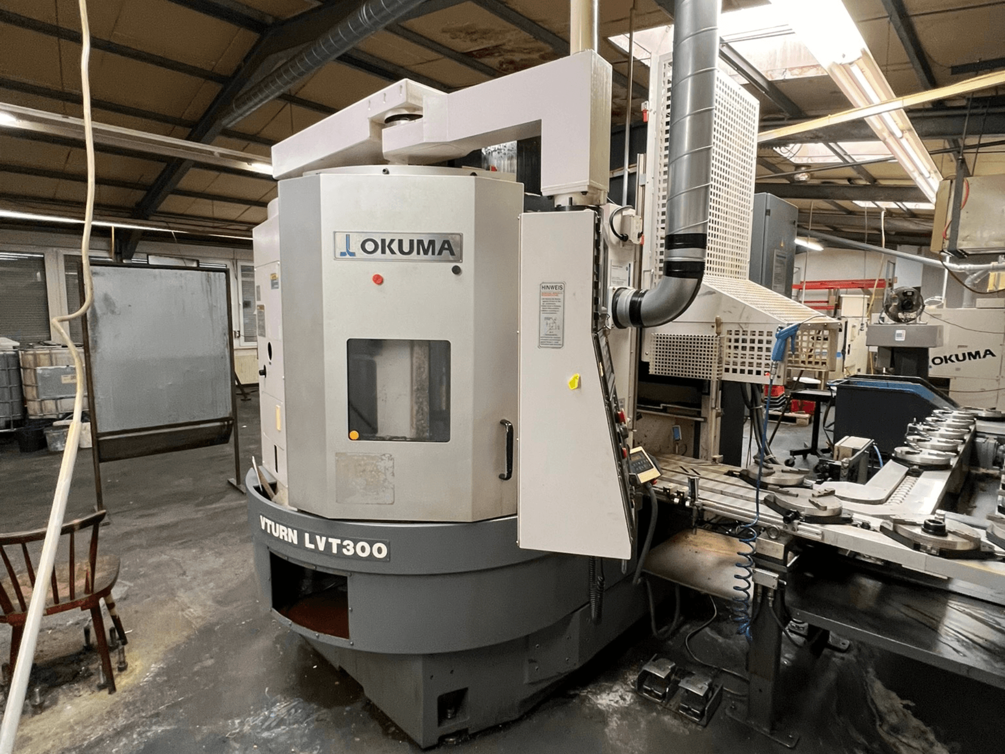 Torno CNC Okuma Vturn LVT300, vista lateral en entorno industrial, mostrando el panel de control y el sistema de refrigerante.