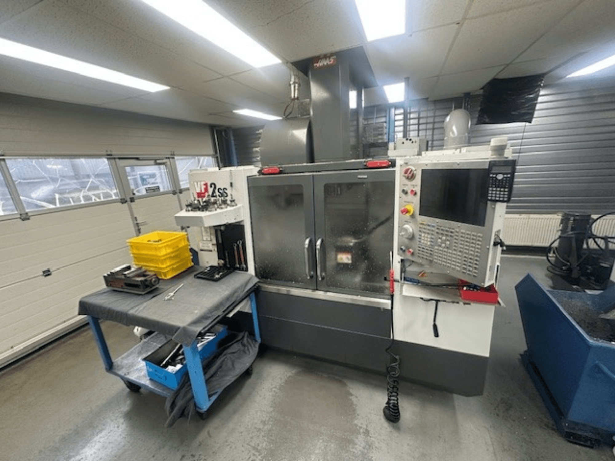 Vista frontal del centro de mecanizado vertical HAAS VF-2SS con panel de control, mesa de trabajo y estación de almacenamiento de herramientas.