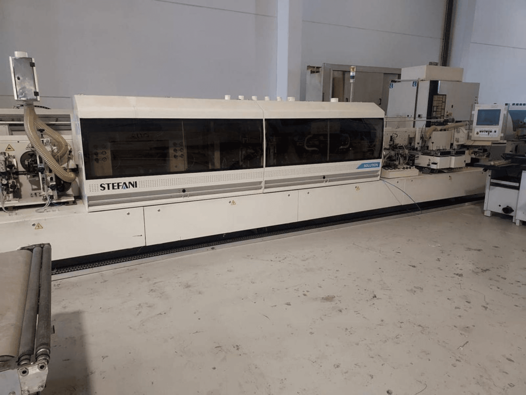 Encoladora de cantos Stefani Solutions, vista frontal, con el sistema de extracción de polvo y el panel de control visibles, en un taller.