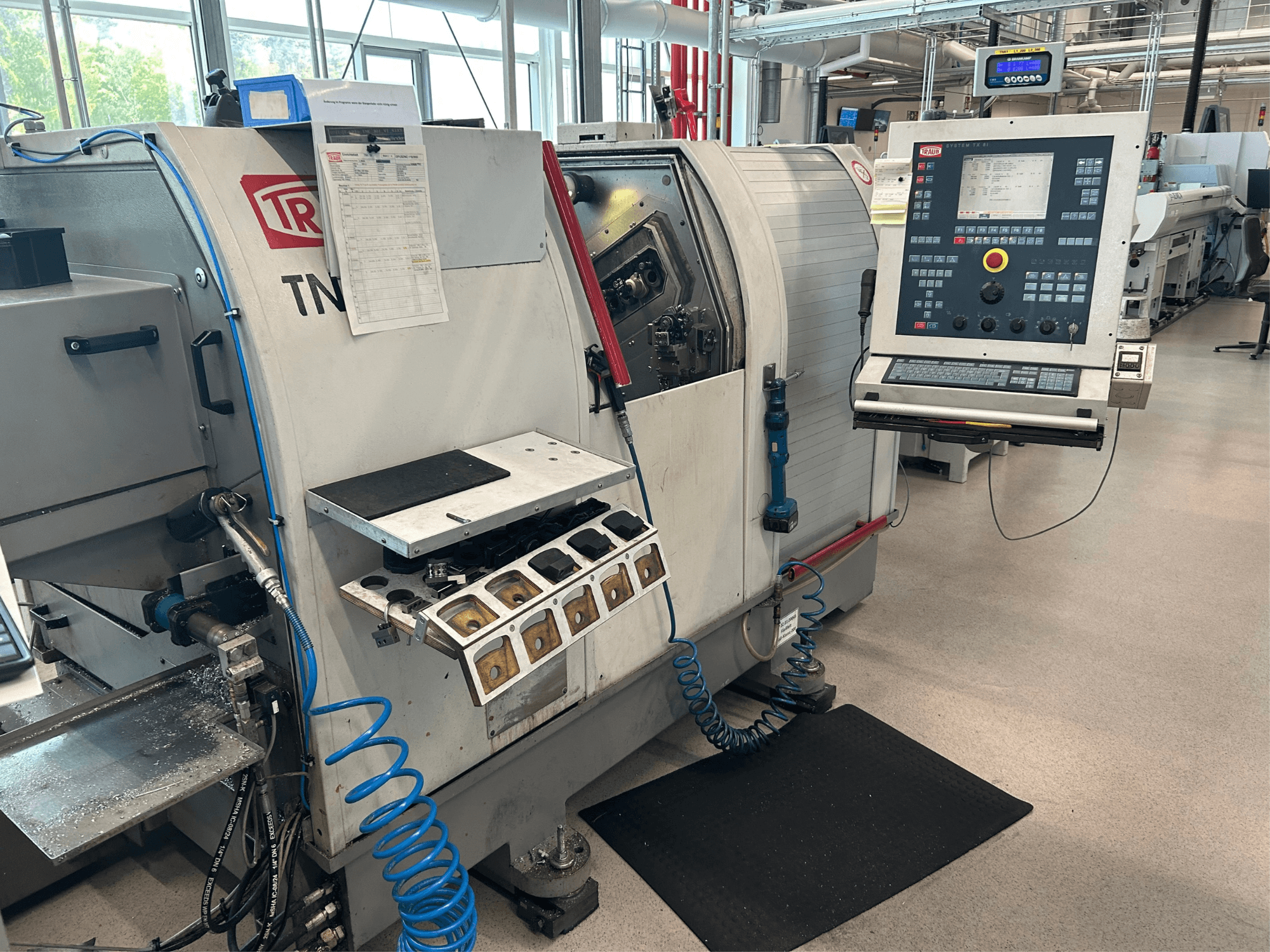 Máquina de torneado horizontal TRAUB TNK 36, vista frontal, mostrando el panel de control, el portaherramientas y el área de trabajo con virutas de metal.